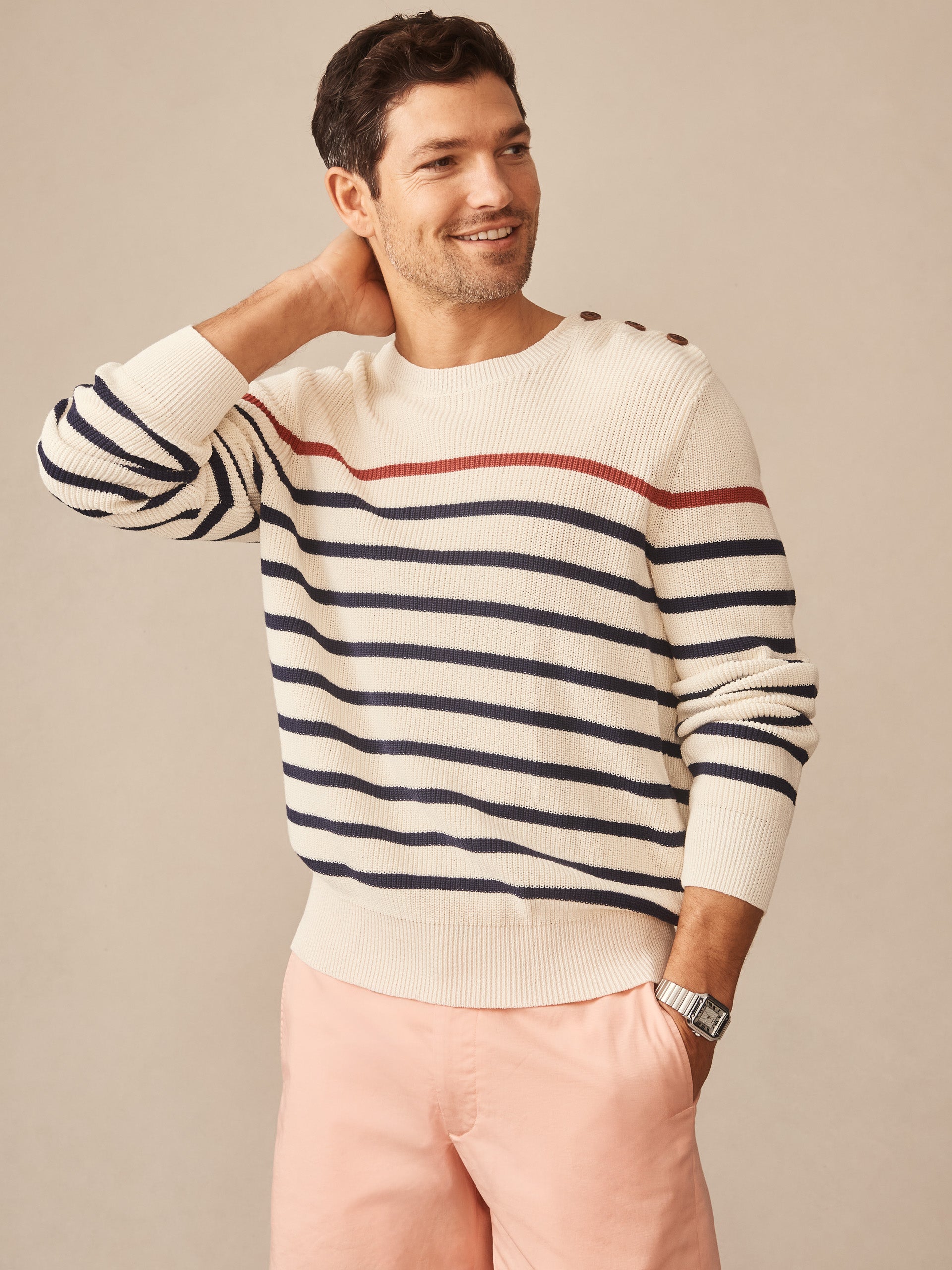 Man wearing J.McLaughlin Bennett Sweater in Stripe with navy and rust stripes on cream, paired with light pink shorts, showcasing effortlessly stylish, enduring designs and innovative fabrics in a legacy of timeless fashion. A destination for defining style. Life, Well-Lived.