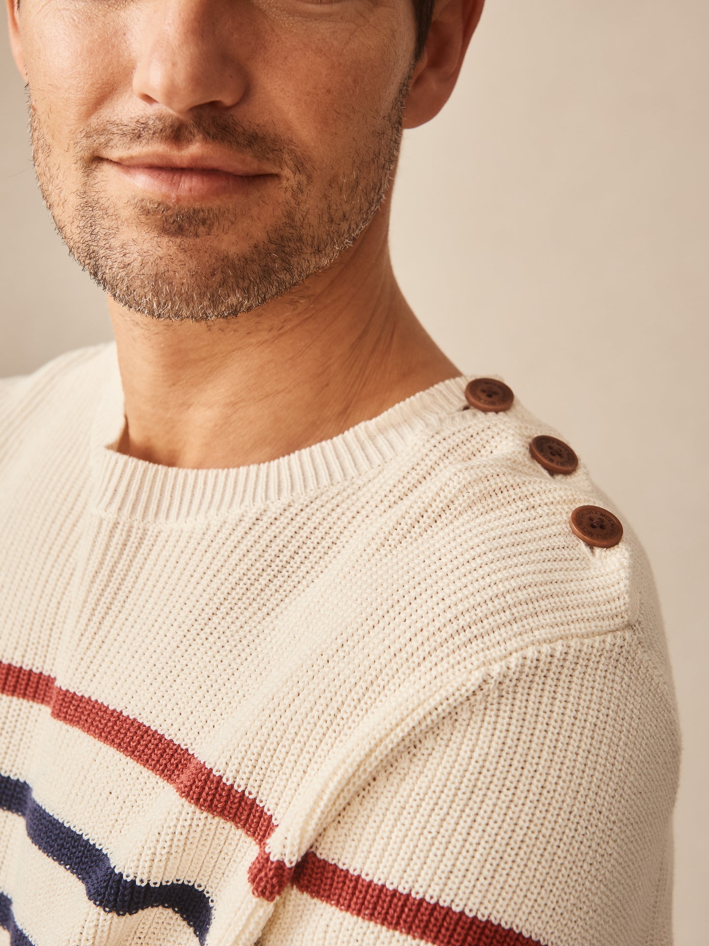 Close-up of a man wearing the Bennett Sweater in Stripe by J.McLaughlin, featuring natural tones with navy and red stripes, wooden buttons on the shoulder, effortlessly stylish and crafted with innovative fabrics. A destination for defining style. Life, Well-Lived.