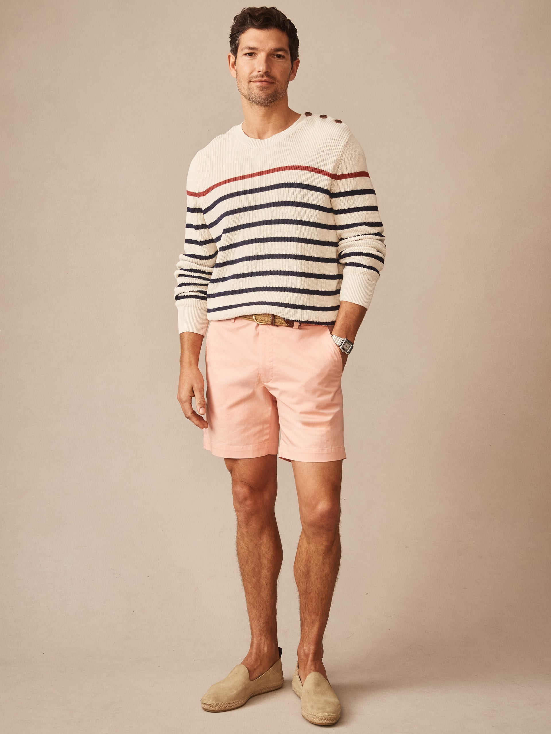 A man wearing a Bennett Sweater in Stripe by J.McLaughlin, featuring off-white with navy and red stripes, styled with pink shorts and beige slip-on shoes, showcasing effortlessly stylish, enduring designs and innovative fabrics from a destination for defining style. Life, Well-Lived.