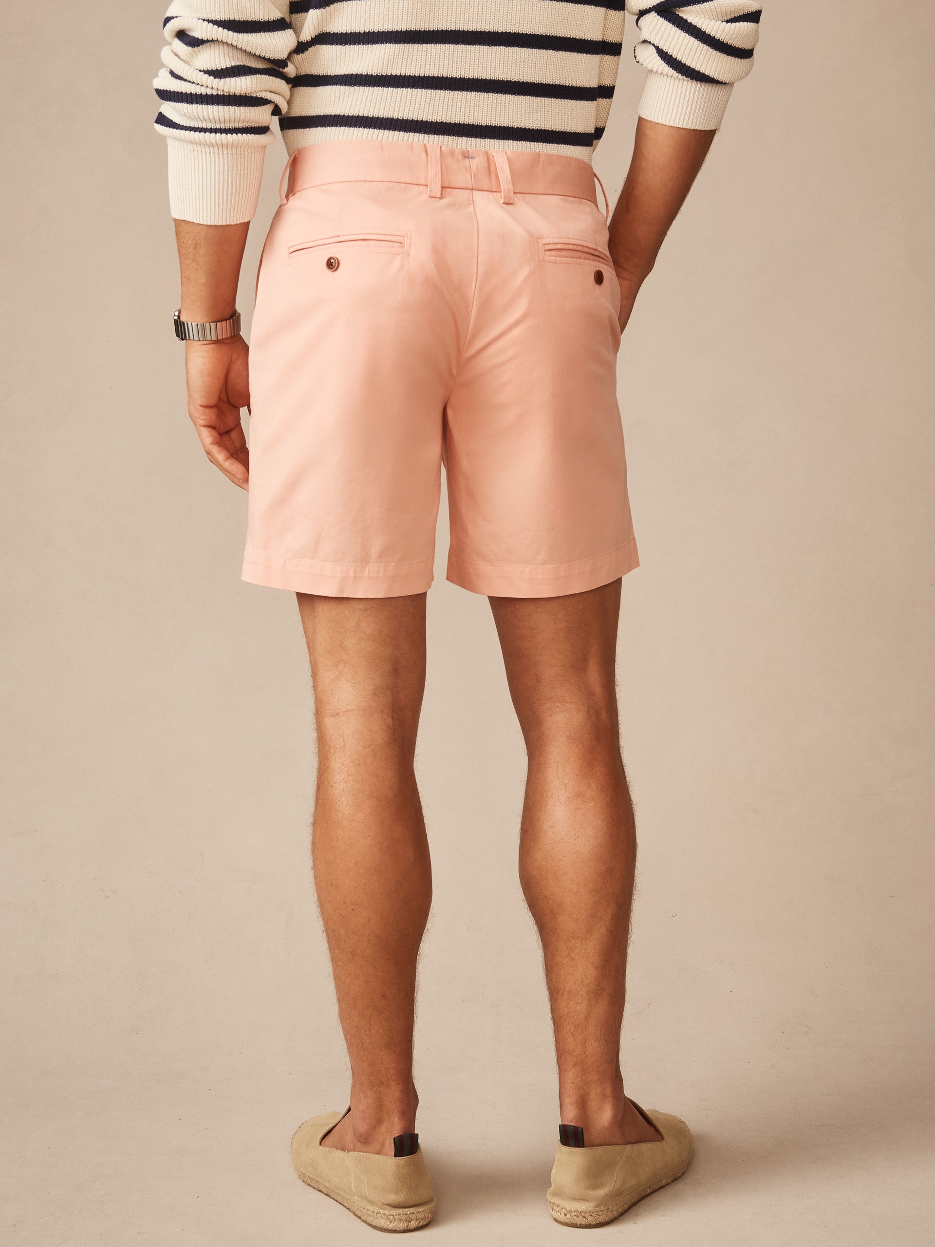 Rear view of a man wearing pink Chatham Shorts by J.McLaughlin paired with a striped sweater and casual slip-on shoes, showcasing effortlessly stylish, enduring designs in innovative fabrics.
