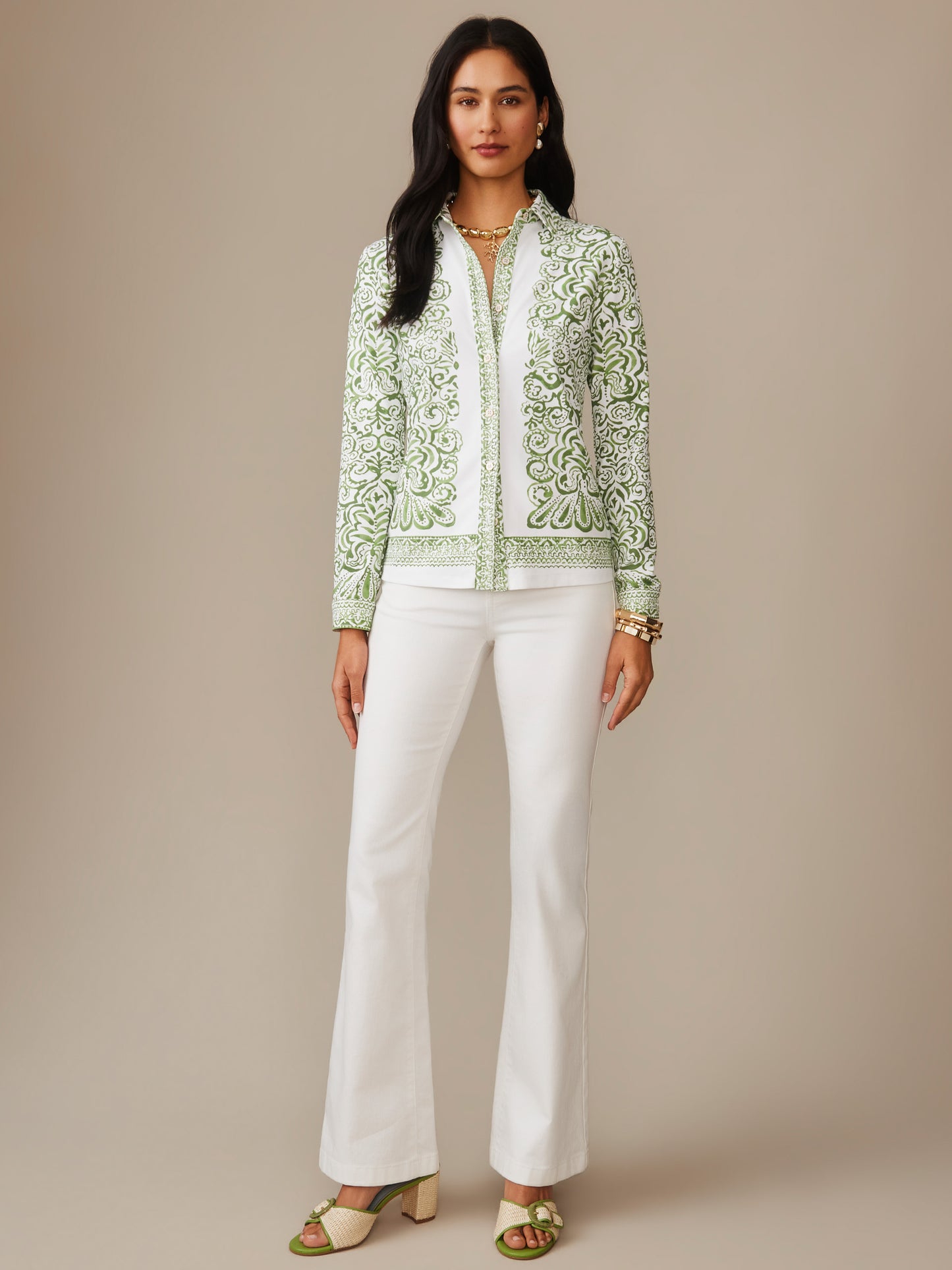 A model wearing the Betty Shirt in Faiz Edge from J.McLaughlin featuring an intricate green and white pattern, paired with white pants and stylish sandals, showcasing effortlessly stylish, enduring designs and innovative fabrics. A destination for defining style. Life, Well-Lived.