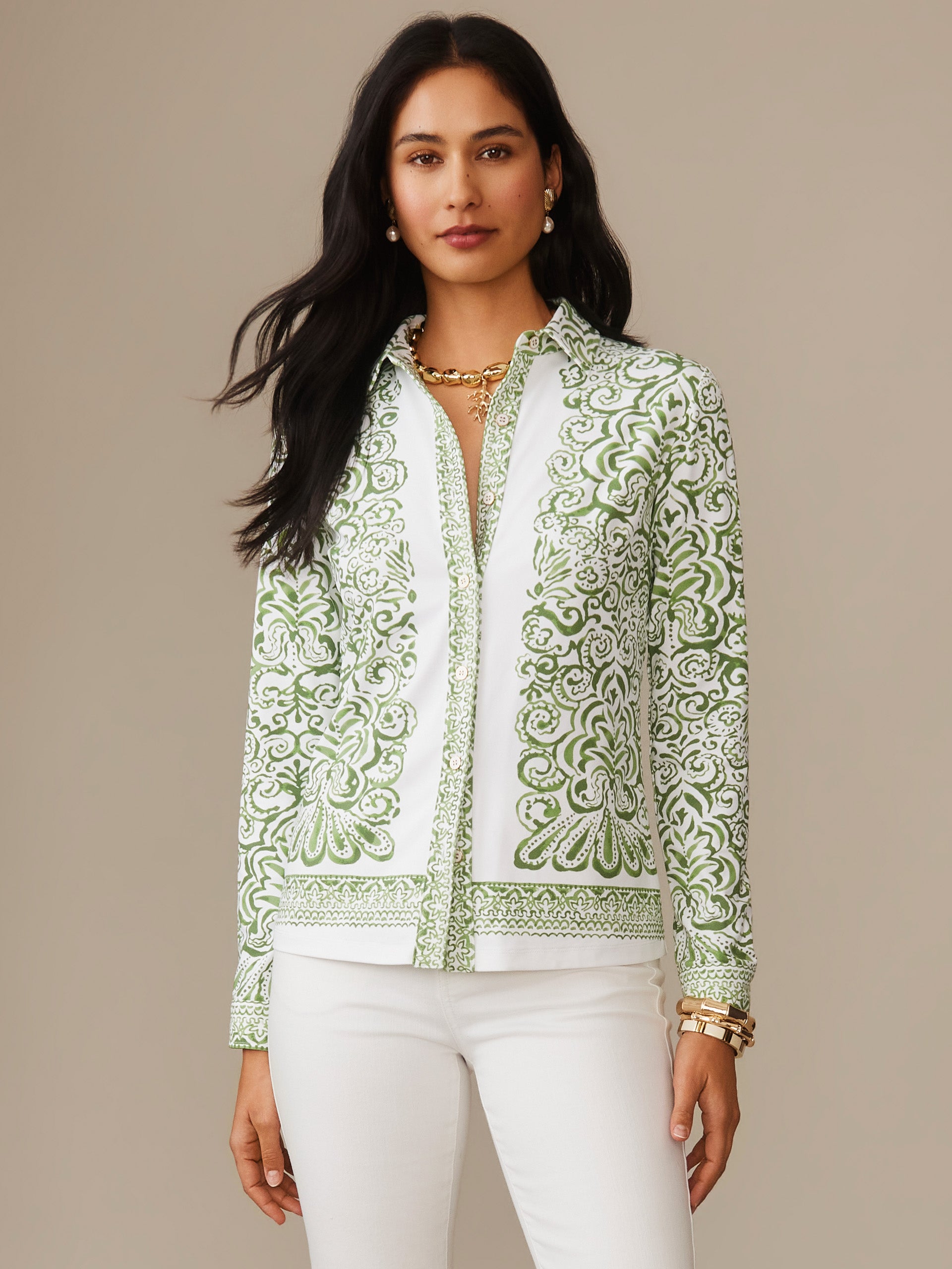 Woman wearing a Betty Shirt in Faiz Edge by J. McLaughlin, featuring an intricate green and white pattern paired with white pants, embodying effortlessly stylish and enduring designs for a life well-lived.