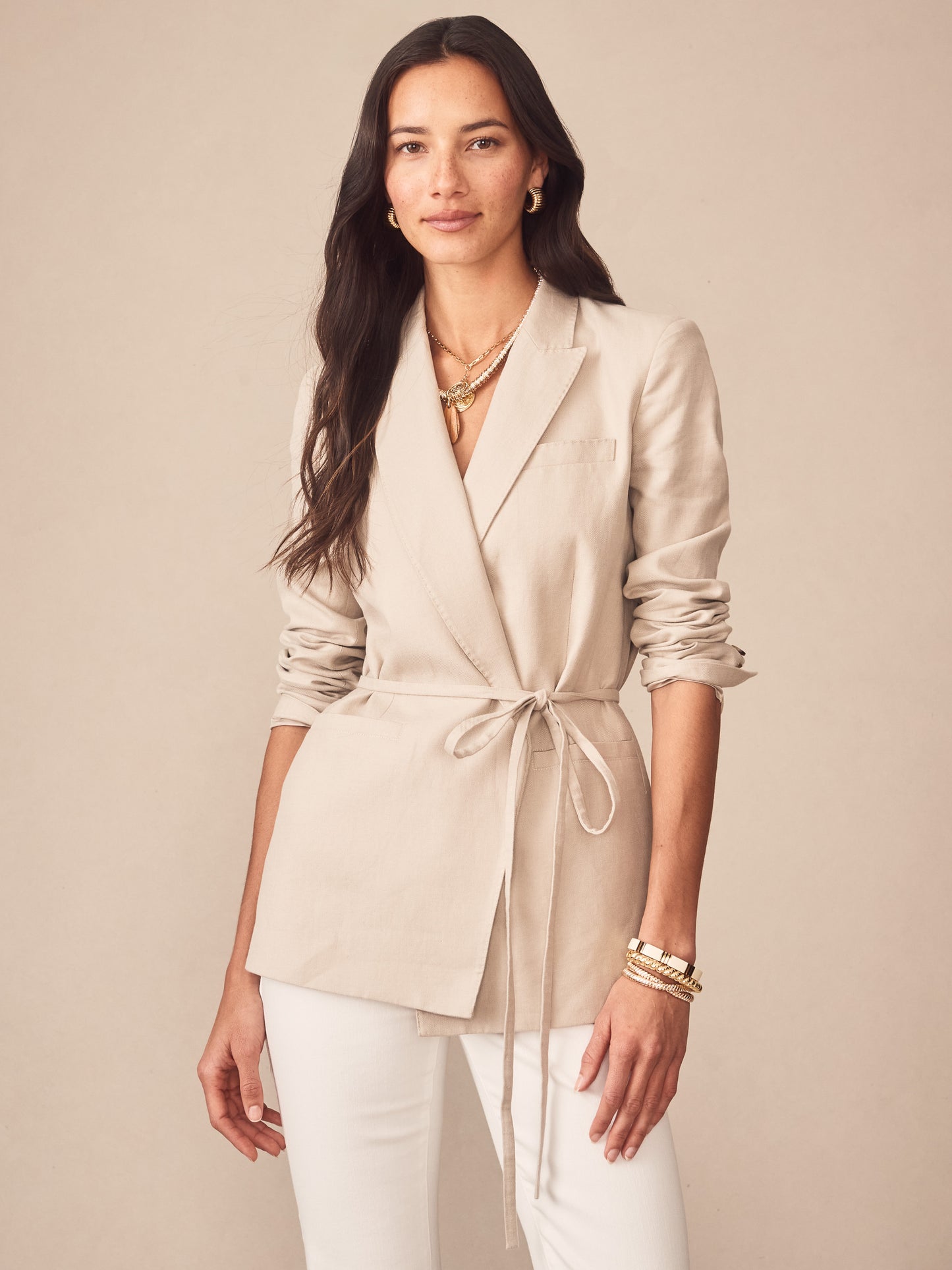 Woman wearing a light beige Biltmore Linen Blend Blazer by J.McLaughlin, styled with rolled sleeves, layered gold necklaces, and bracelets for an effortlessly stylish, enduring design.