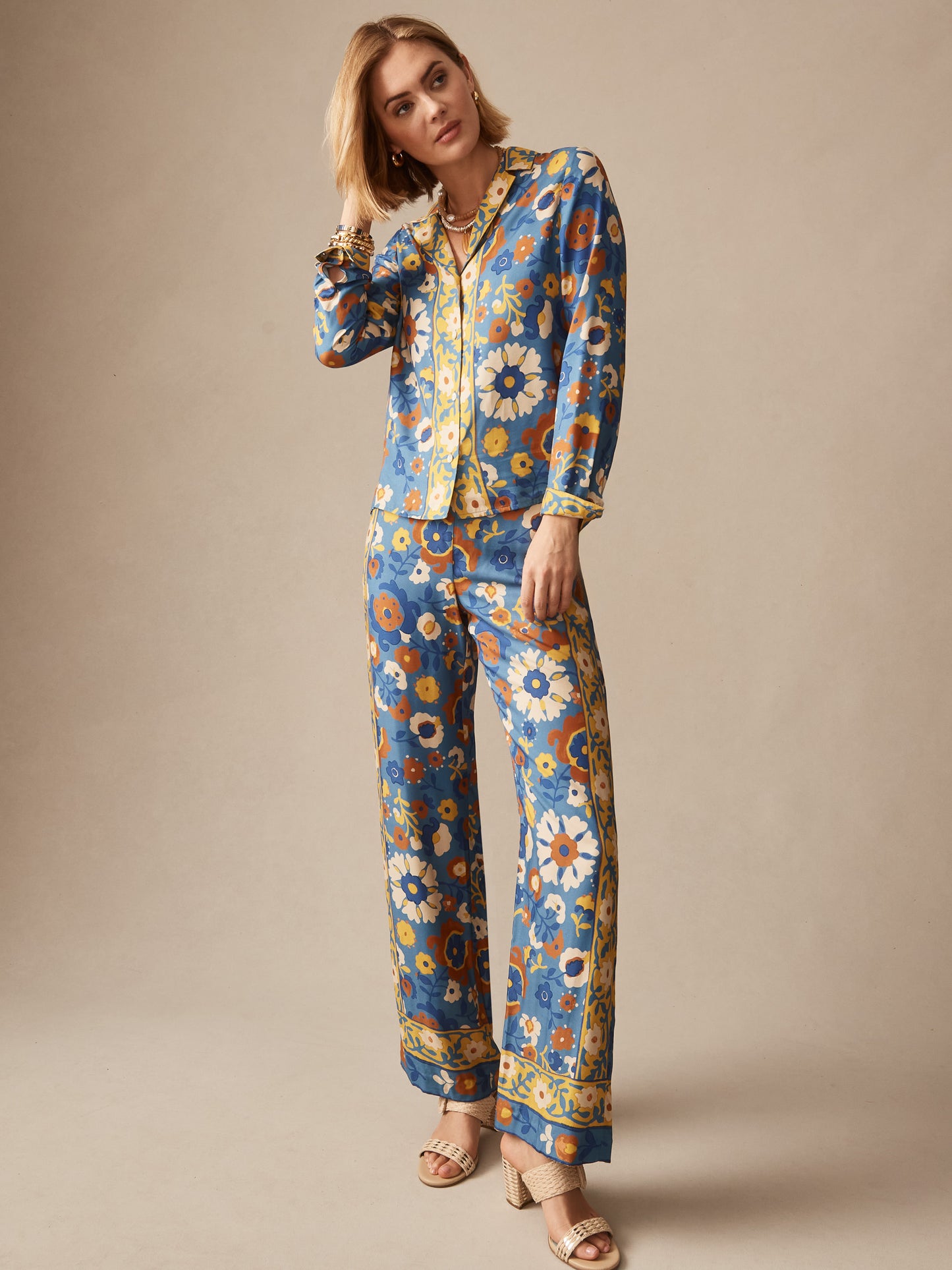 Woman wearing J.McLaughlin Carter Silk Blend Pants in Floral Daydream Edge with matching top, featuring vibrant floral patterns on a blue background, embodying effortlessly stylish and enduring designs. A destination for defining style. Life, Well-Lived.