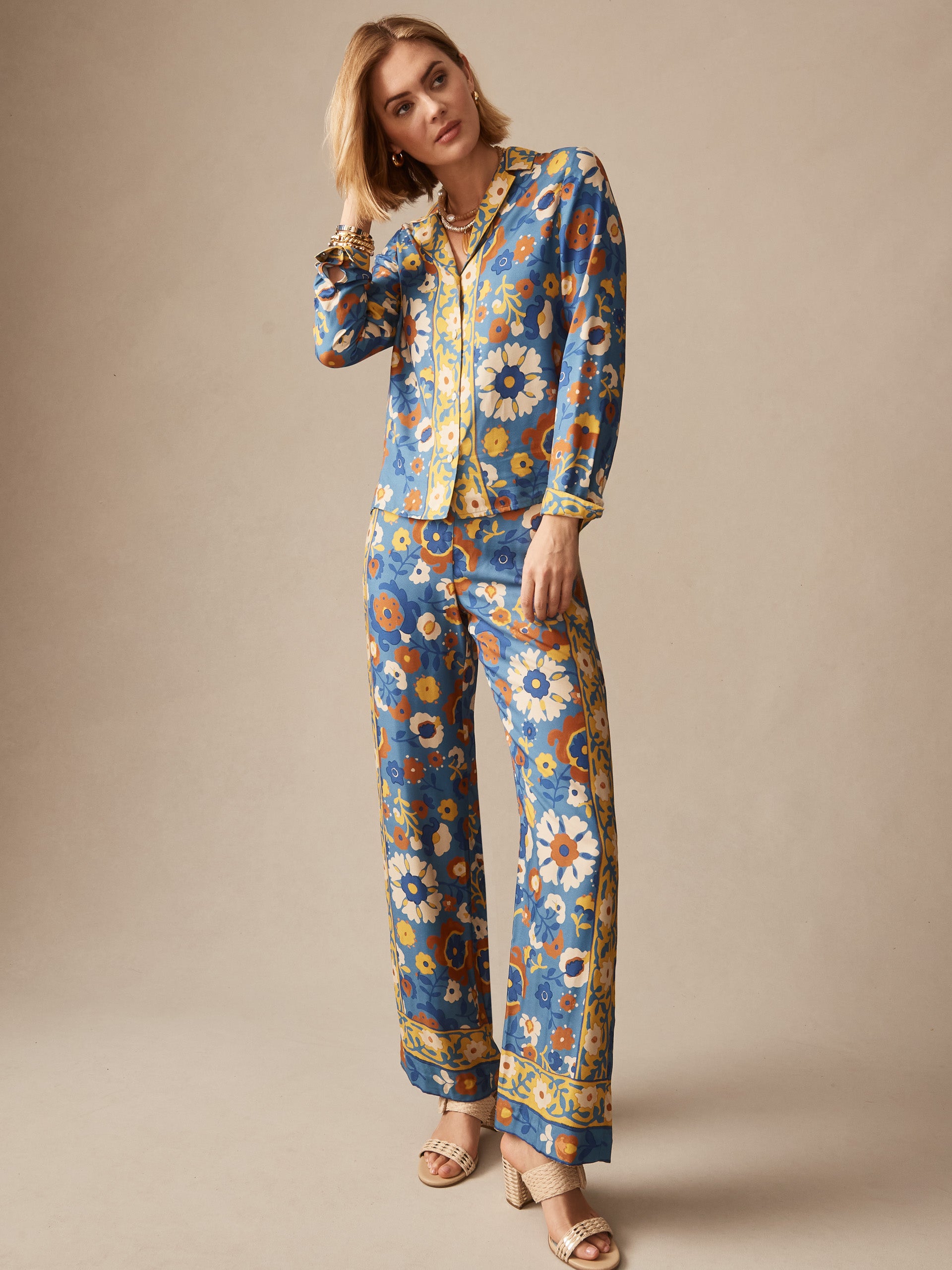 Woman wearing J.McLaughlin Carter Silk Blend Pants in Floral Daydream Edge with matching top, featuring vibrant floral patterns on a blue background, embodying effortlessly stylish and enduring designs. A destination for defining style. Life, Well-Lived.