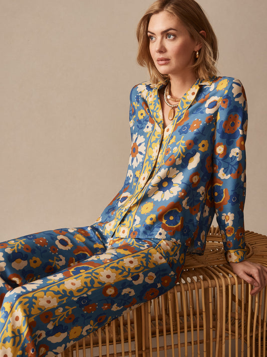Woman seated on rattan bench wearing the Bimini Shirt in Floral Daydream Edge by J.McLaughlin, showcasing effortlessly stylish, enduring designs with innovative fabrics.
