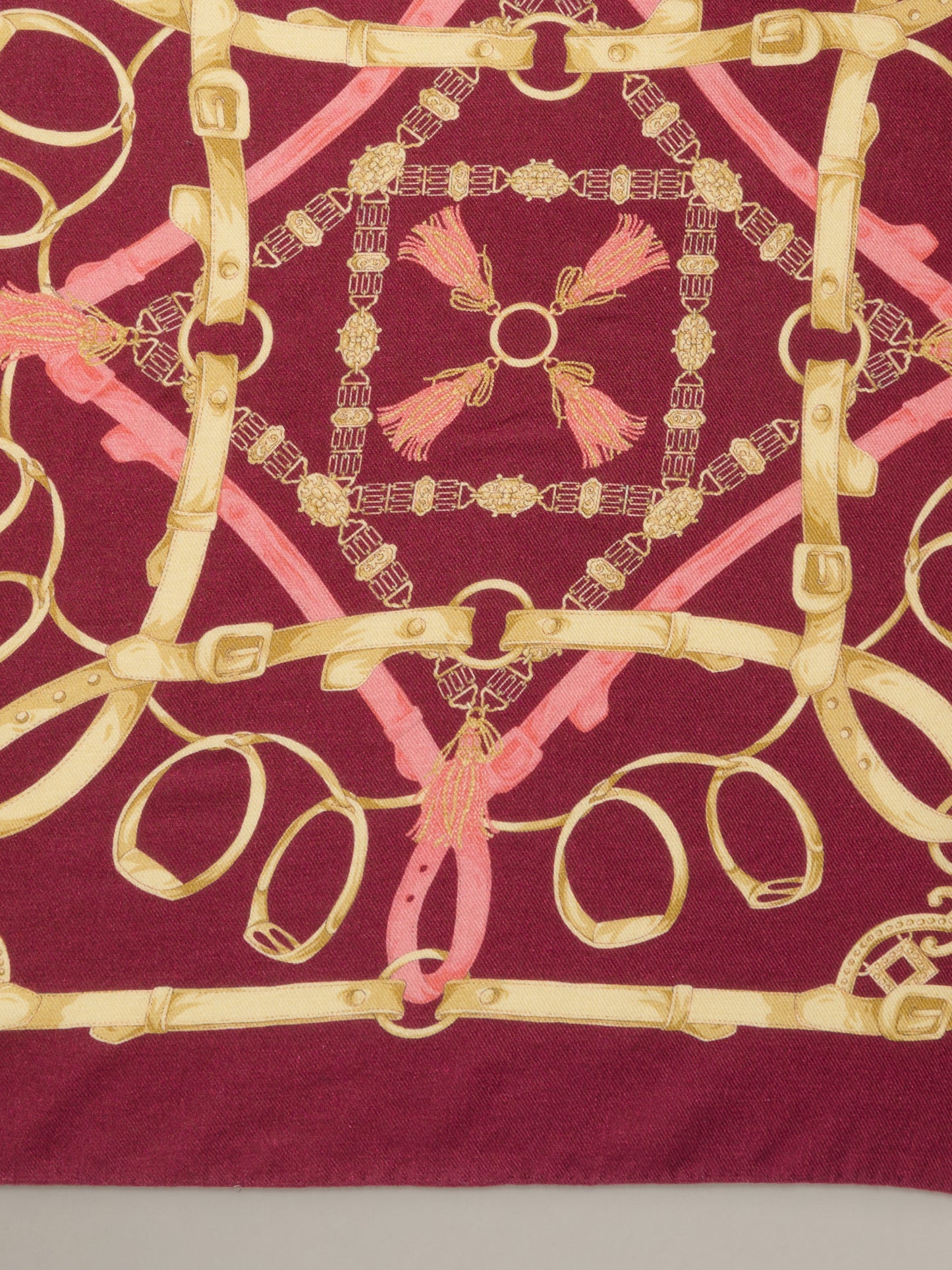The Blair Scarf in Grand Heraldic Corner by J.McLaughlin shown in burgundy with ornate pink and gold heraldic belt and chain motifs