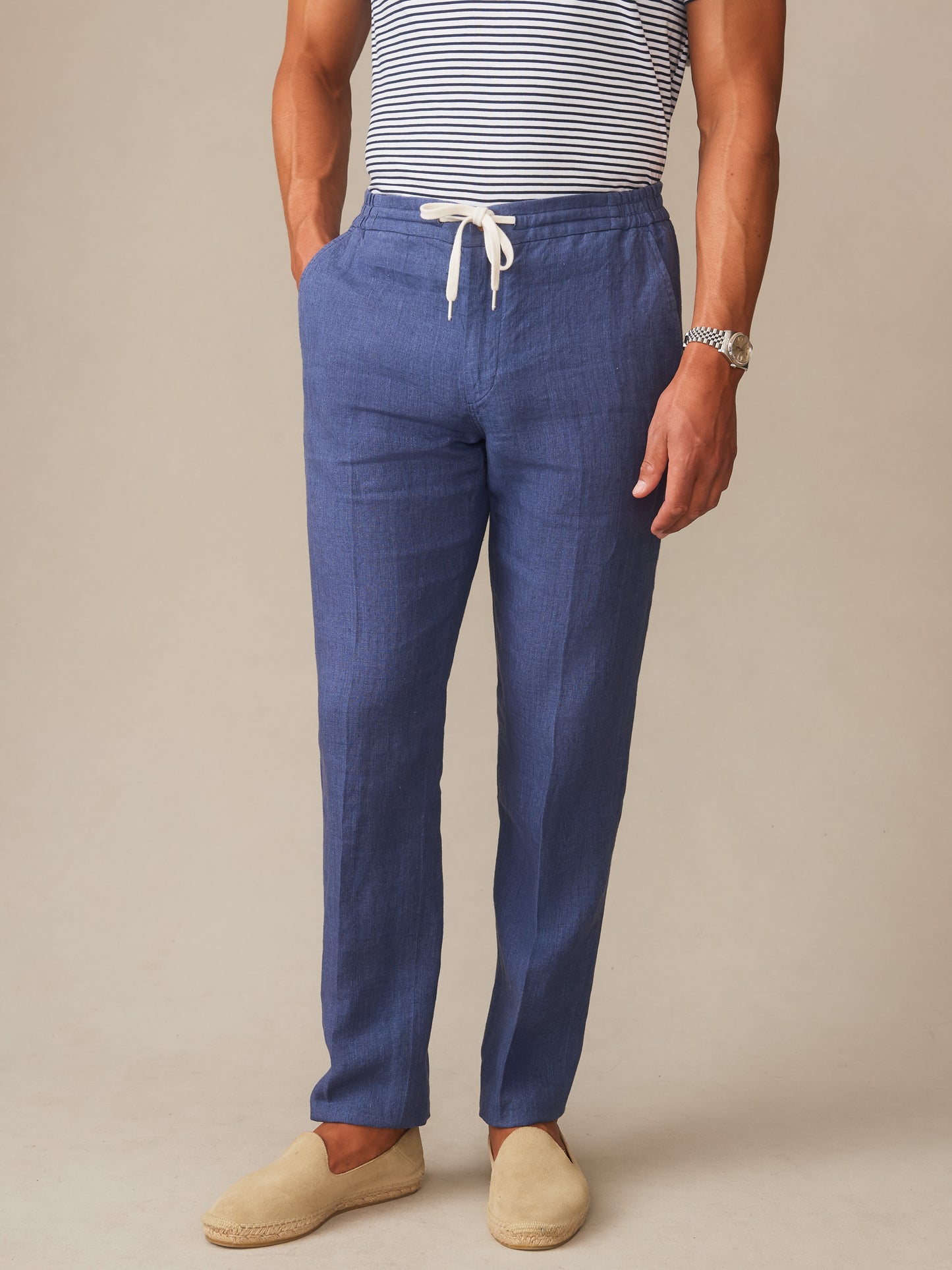 Man wearing Bleeker Linen Fancy Pants in deep blue by J.McLaughlin, styled with a striped shirt and casual slip-on shoes, showcasing effortlessly stylish, enduring designs with a legacy of timeless fashion.