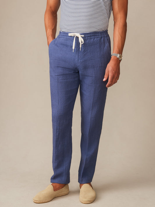 Man wearing Bleeker Linen Fancy Pants in deep blue by J.McLaughlin, styled with a striped shirt and casual slip-on shoes, showcasing effortlessly stylish, enduring designs with a legacy of timeless fashion.
