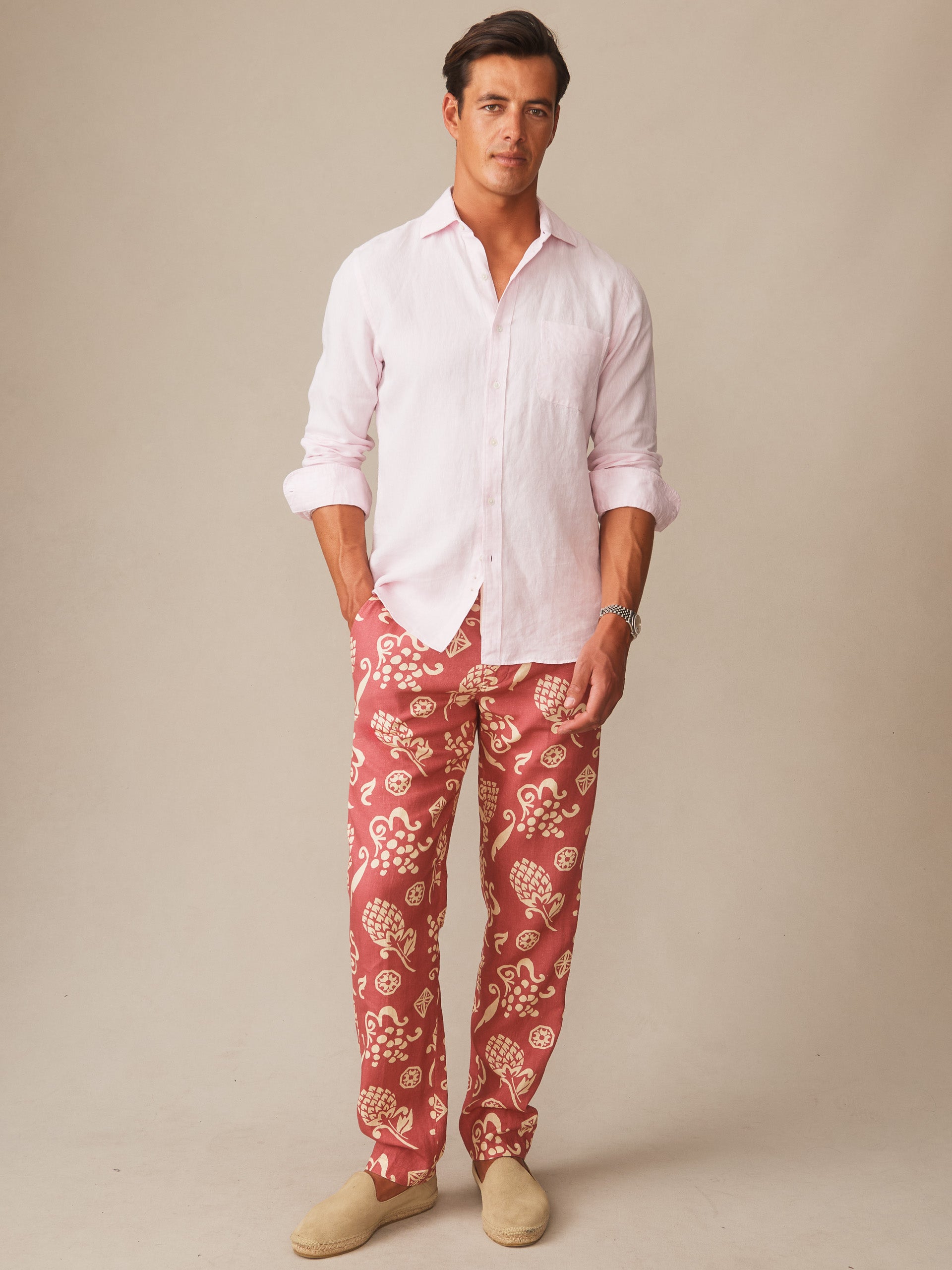 Man wearing Bleeker Linen Fancy Pants in Corallo Bloom by J.McLaughlin paired with a light pink linen shirt and beige slip-on shoes, showcasing effortlessly stylish, enduring designs with innovative fabrics in a legacy of timeless fashion at a destination for defining style. Life, Well-Lived.