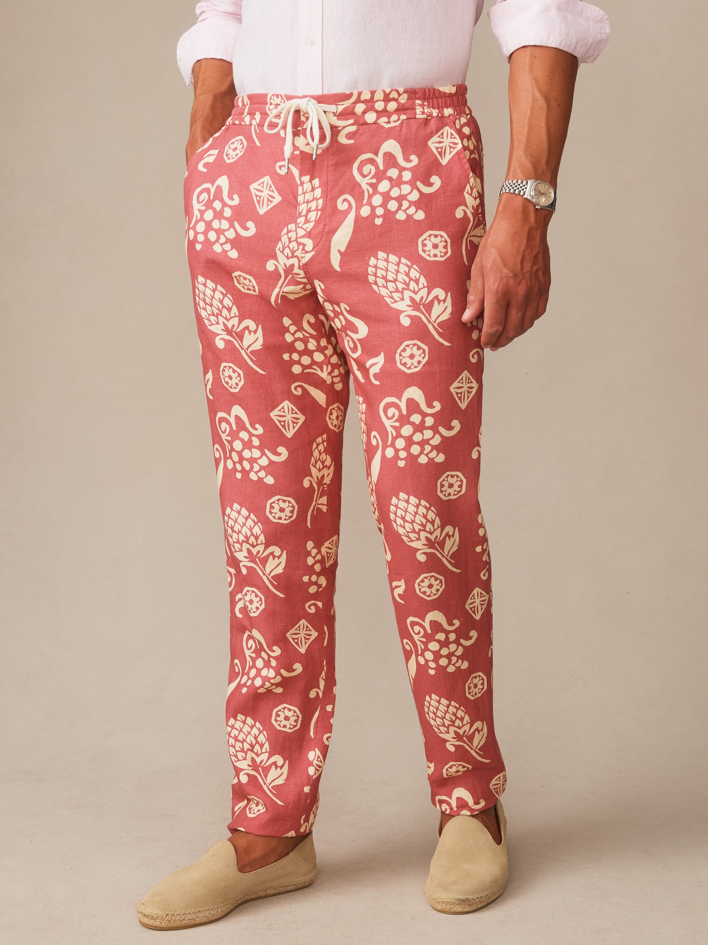 Man wearing Bleeker Linen Fancy Pants in Corallo Bloom with coral and cream botanical pattern, styled with light shirt and slip-on shoes by J.McLaughlin, showcasing effortlessly stylish, enduring designs in innovative fabrics. A destination for defining style. Life, Well-Lived.