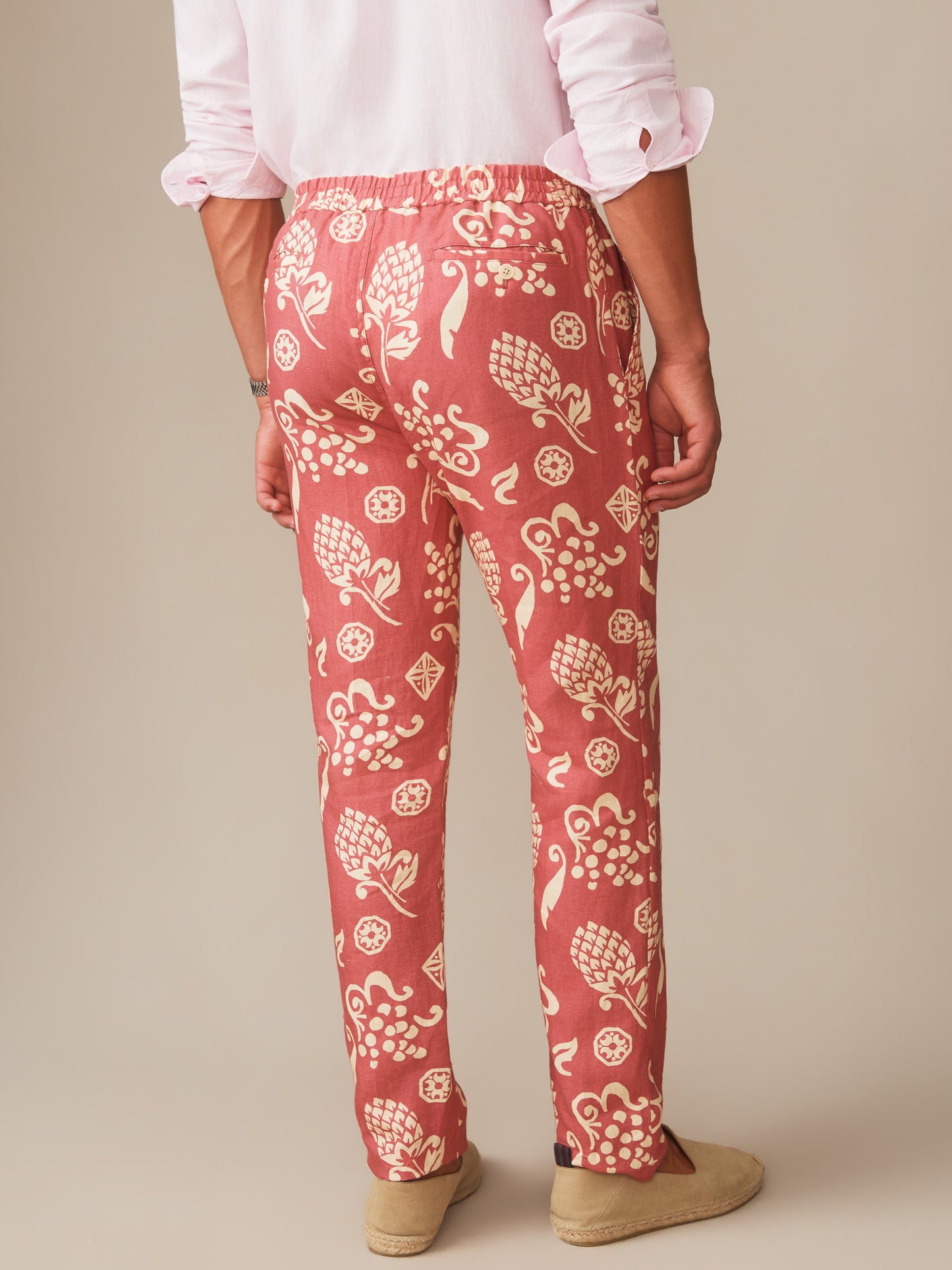 Back view of a person wearing Bleeker Linen Fancy Pants in Corallo Bloom by J.McLaughlin, featuring a coral linen fabric with cream botanical prints, styled with a rolled-up white shirt and casual shoes. Effortlessly stylish, enduring designs crafted from innovative fabrics, upholding a legacy of timeless fashion. A destination for defining style. Life, Well-Lived.