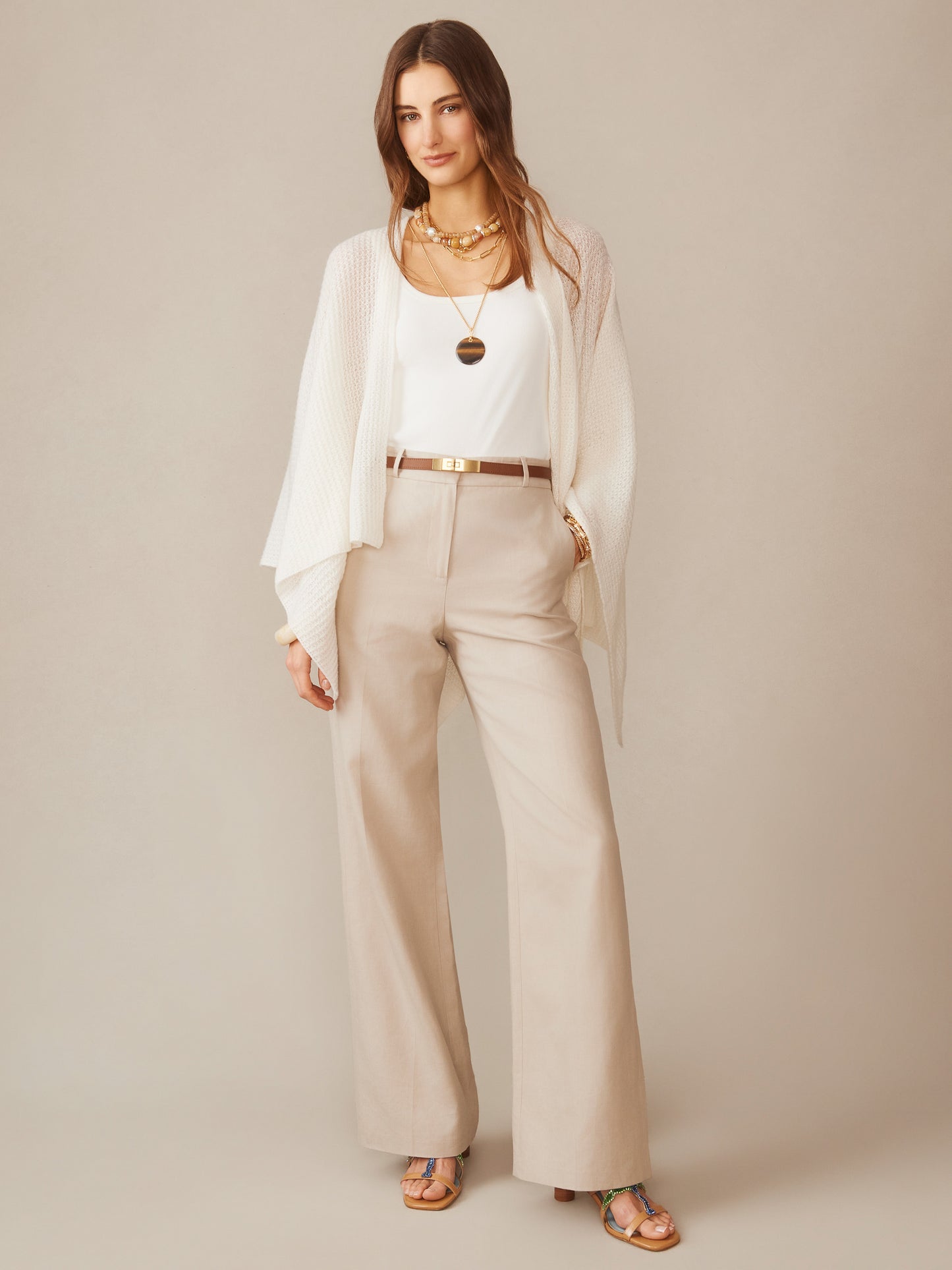 Woman wearing a cream Julianne Cashmere Wrap by J.McLaughlin over a white top and beige pants, styled with layered necklaces and strappy sandals, showcasing effortlessly stylish, enduring designs.