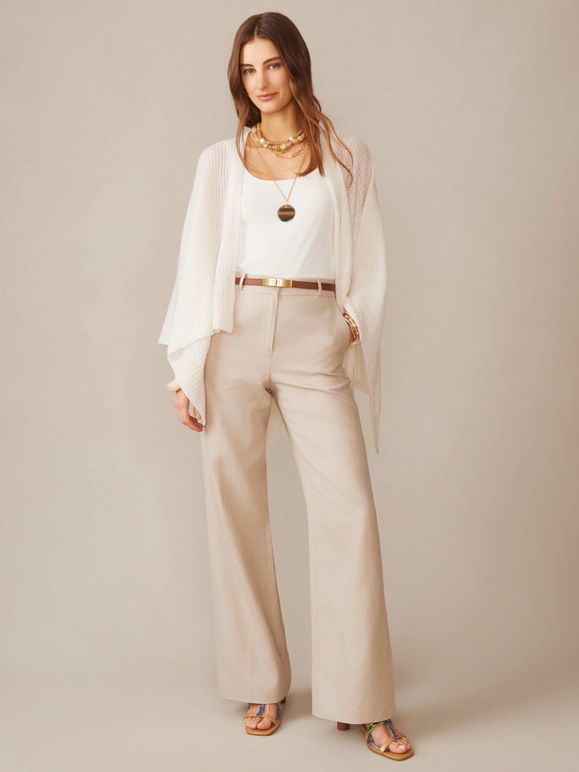 Woman wearing a cream Julianne Cashmere Wrap by J.McLaughlin over a white top and beige pants, styled with layered necklaces and strappy sandals, showcasing effortlessly stylish, enduring designs.