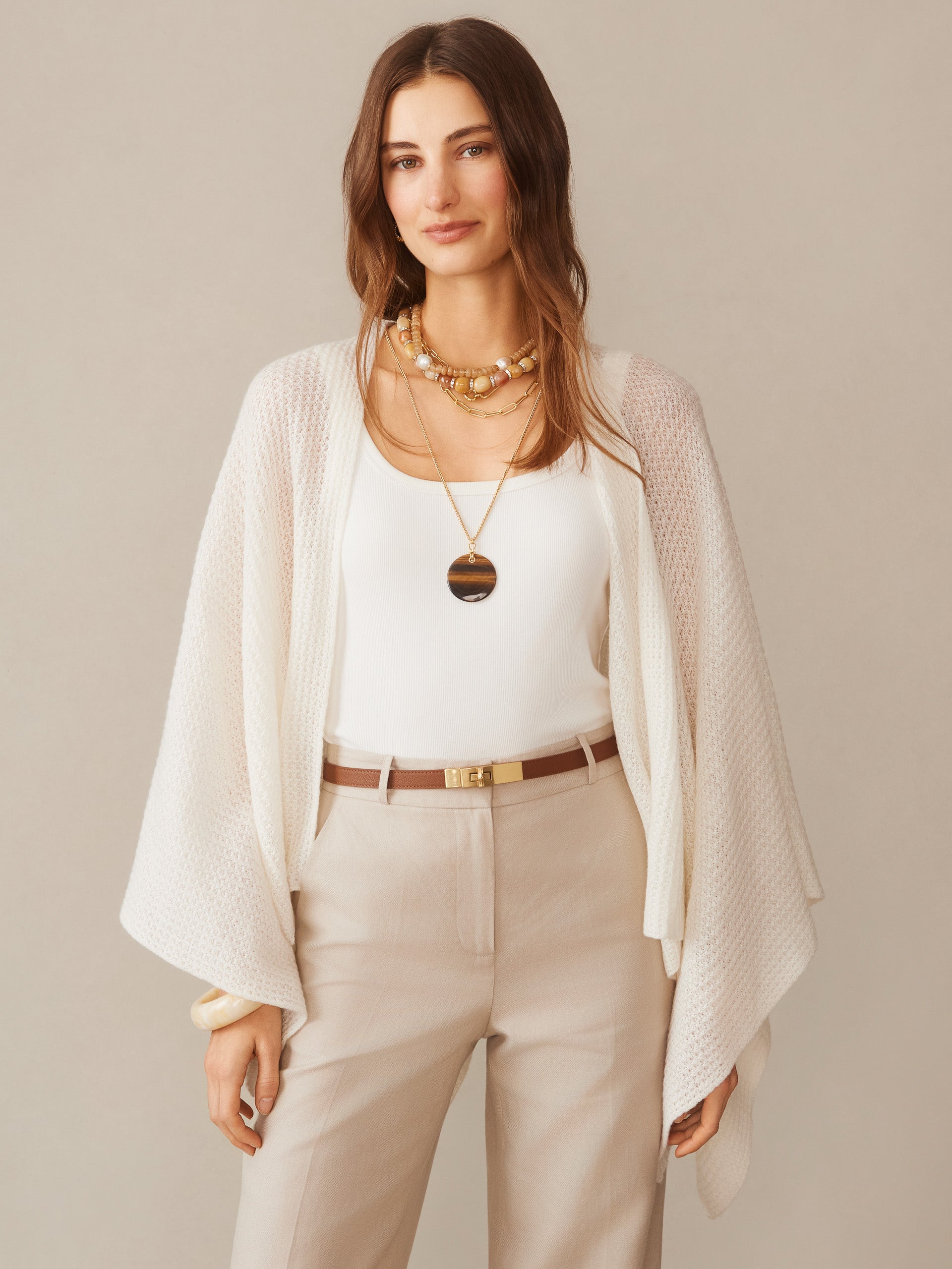 Woman wearing a cream Julianne Cashmere Wrap over a white top and beige pants, styled with layered necklaces and a tan belt, showcasing J.McLaughlin’s effortlessly stylish, enduring designs.