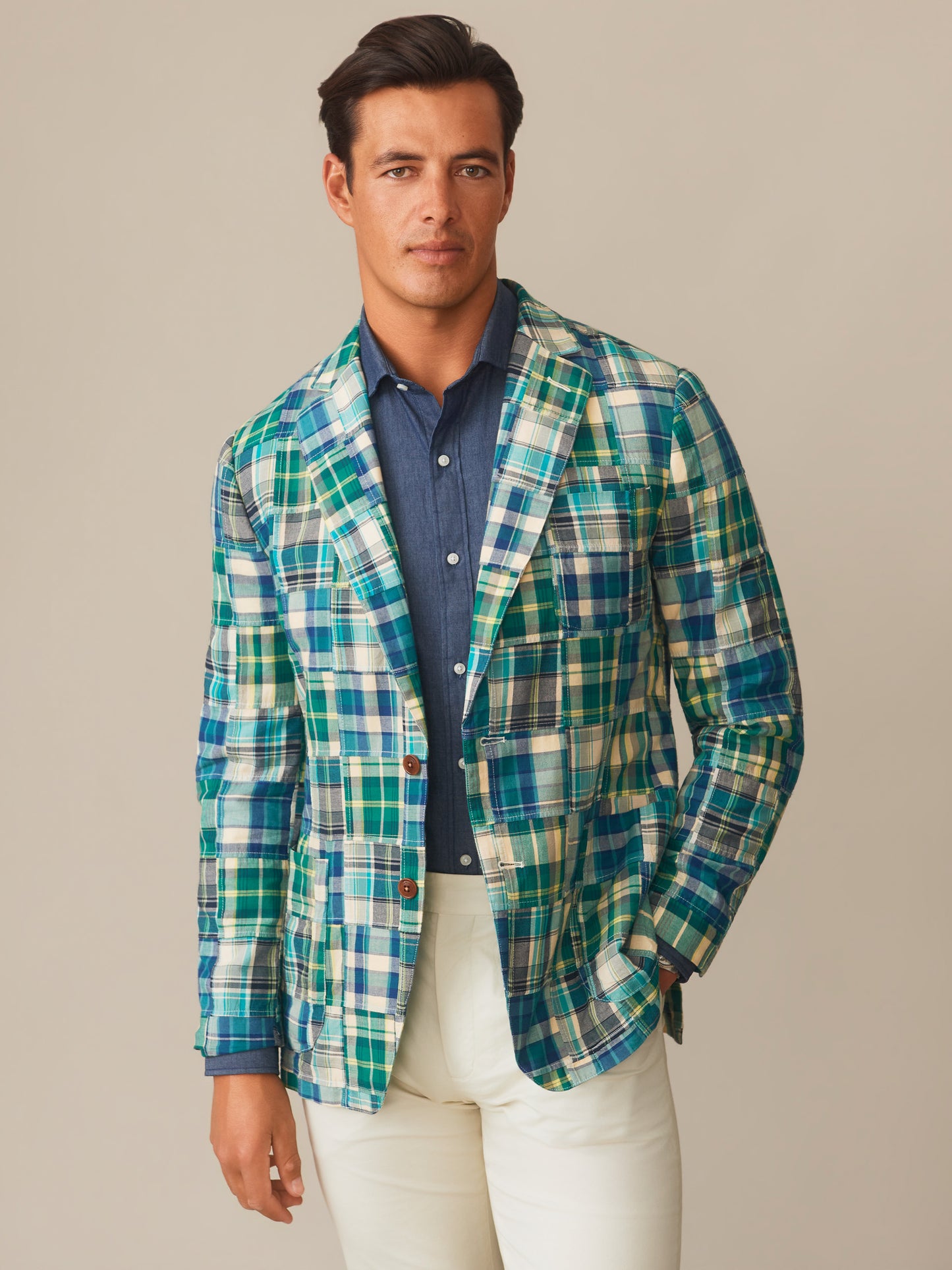 A man wearing the Brera Sport Coat in Patchwork by J.McLaughlin in green and blue plaid over a navy shirt and white pants, embodying effortlessly stylish, enduring designs with innovative fabrics. A destination for defining style. Life, Well-Lived.