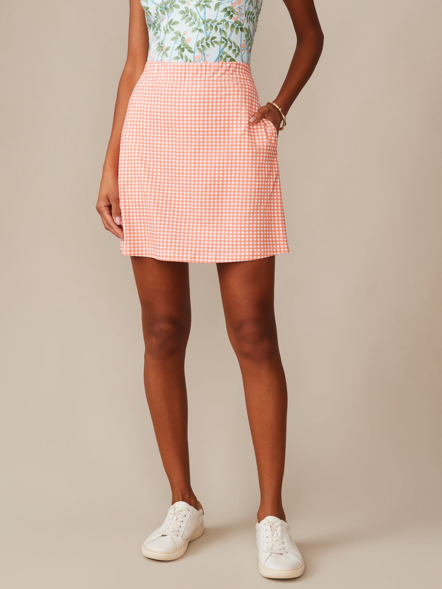 Model wearing J.McLaughlin Briana Skort in Midi Cabana Gingham in coral and white, paired with casual white sneakers, showcasing effortlessly stylish, enduring designs and innovative fabrics from a destination for defining style. Life, Well-Lived.