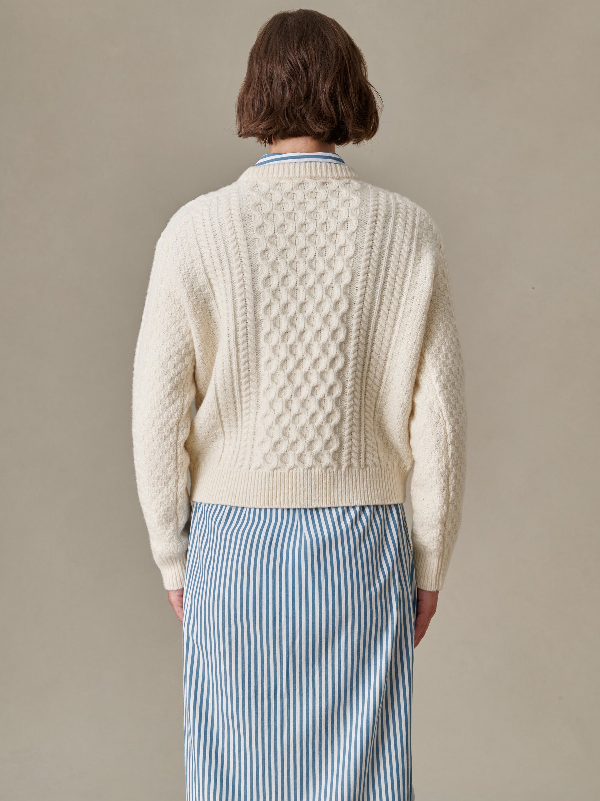 Back view of a person wearing a textured cream Brigette Sweater by J.McLaughlin paired with a blue and white striped skirt, showcasing classic and enduring design.
