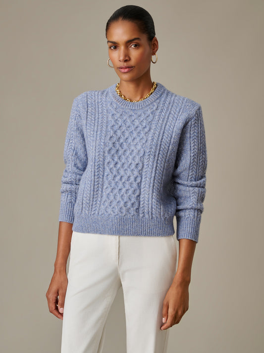 Woman wearing a light blue Brigette Sweater by J.McLaughlin featuring a classic cable knit design, paired with white pants, epitomizing timeless style and quality craftsmanship.