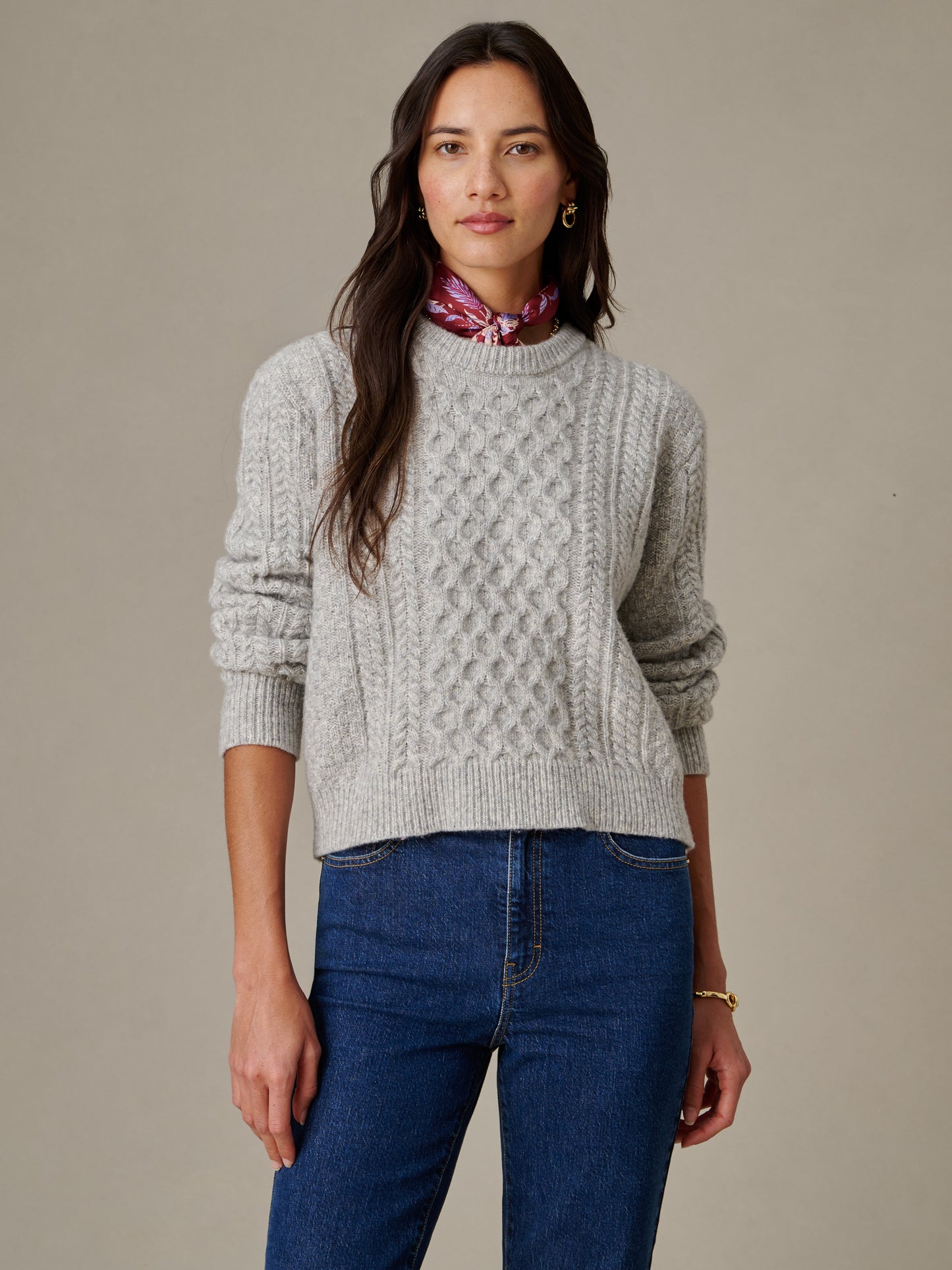 A woman wearing the Brigette Sweater by J.McLaughlin, featuring a textured knit design in a timeless, effortlessly stylish look paired with blue jeans and a red scarf, embodying enduring designs and a legacy of timeless fashion.