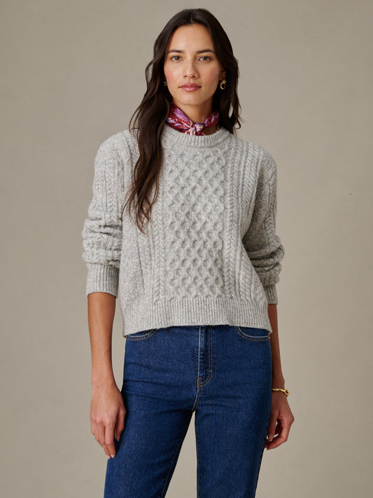 A woman wearing the Brigette Sweater by J.McLaughlin, featuring a textured knit design in a timeless, effortlessly stylish look paired with blue jeans and a red scarf, embodying enduring designs and a legacy of timeless fashion.