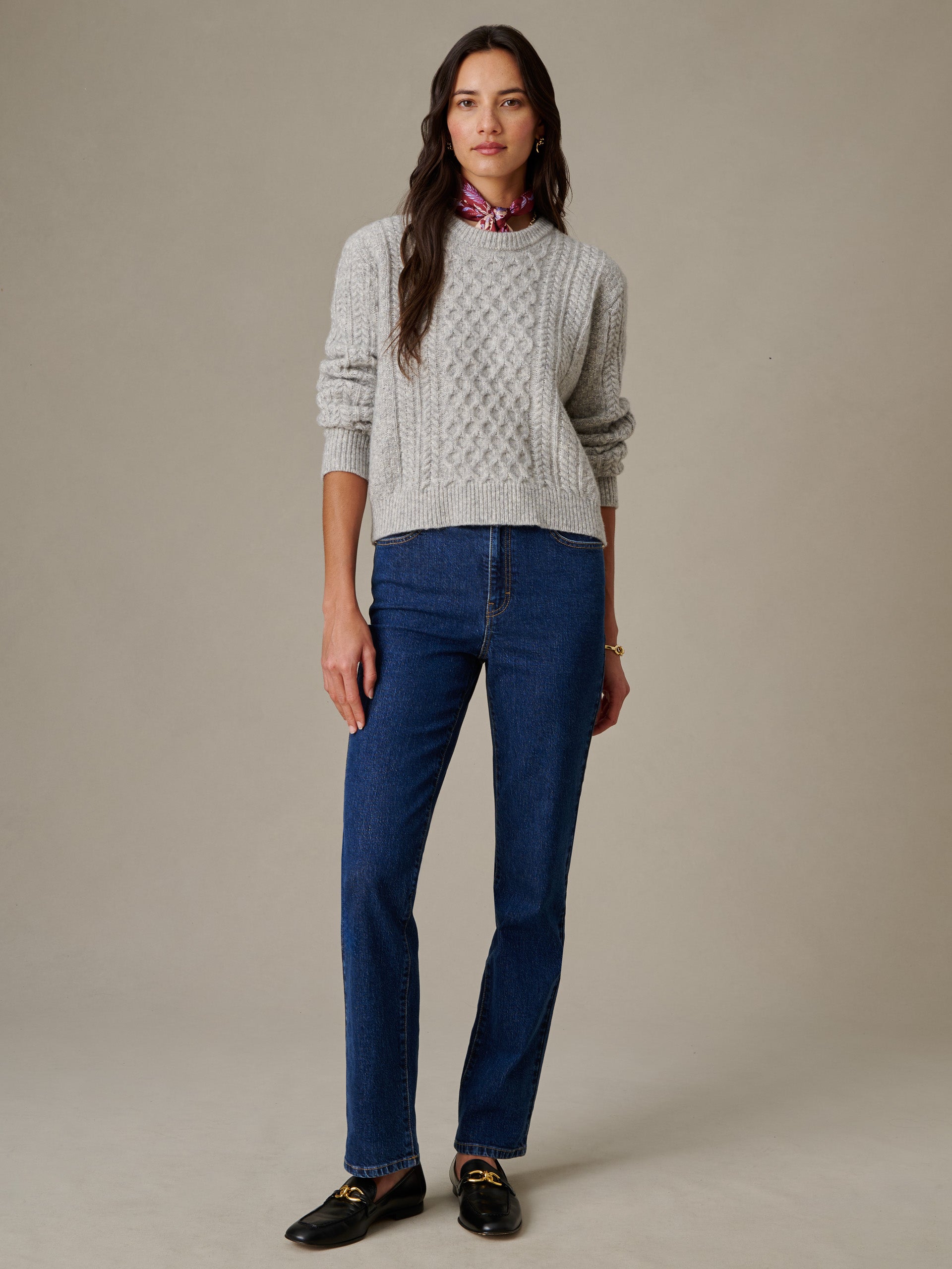 Woman wearing a gray Brigette Sweater by J.McLaughlin paired with blue jeans and black loafers, showcasing effortlessly stylish and enduring designs for timeless fashion.