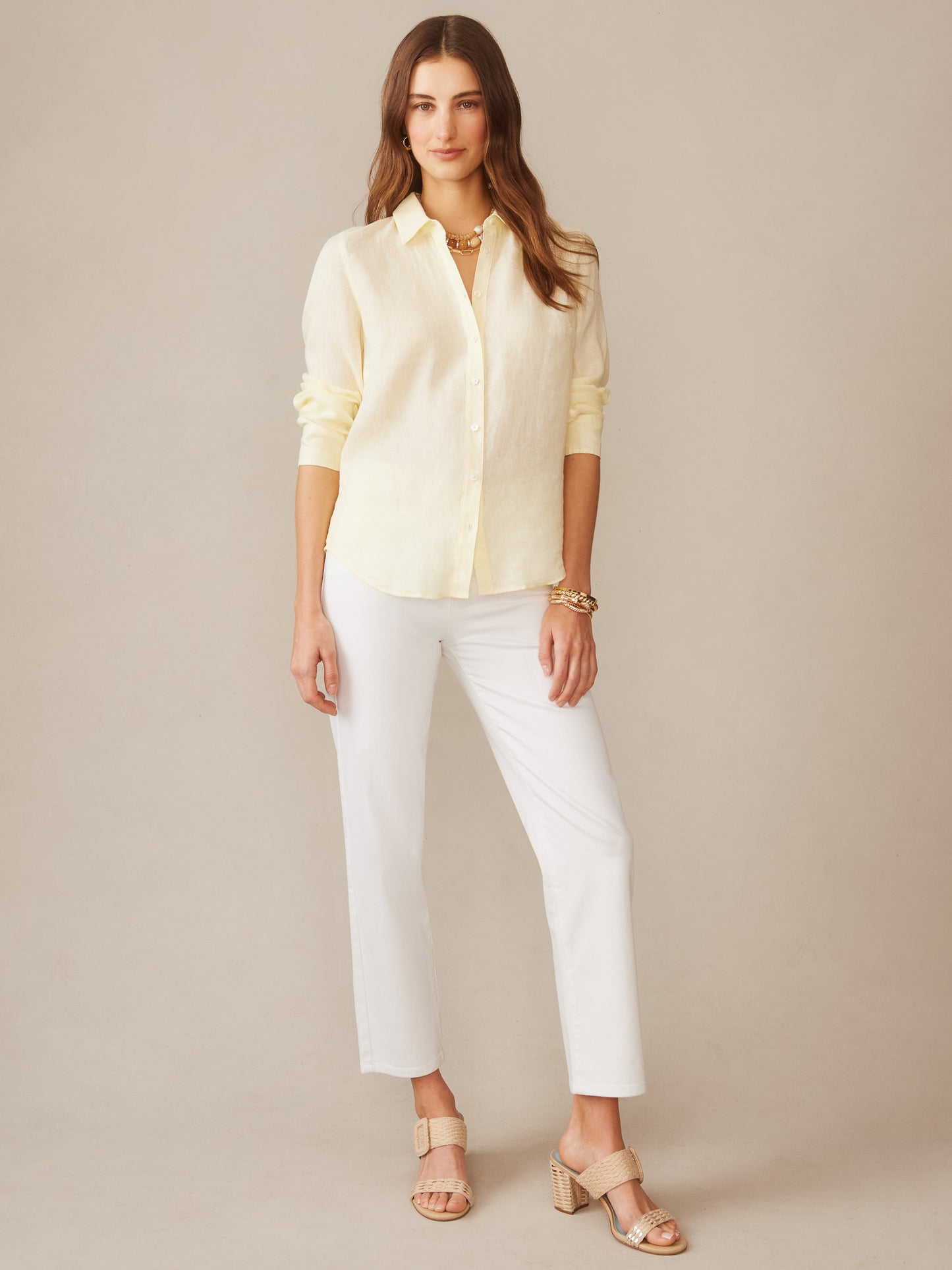 Woman wearing a lemon-colored Britt Linen Shirt by J.McLaughlin paired with white pants and neutral heeled sandals, showcasing effortlessly stylish and enduring designs in timeless fashion.