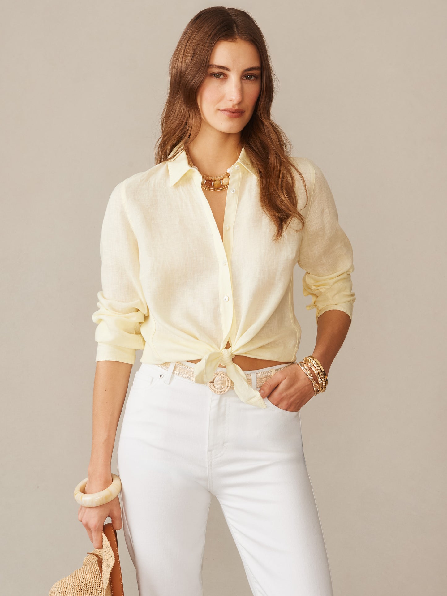 Woman wearing a lemon yellow Britt Linen Shirt by J.McLaughlin, styled with white pants and accessories, showcasing effortlessly stylish, enduring designs in innovative fabrics.