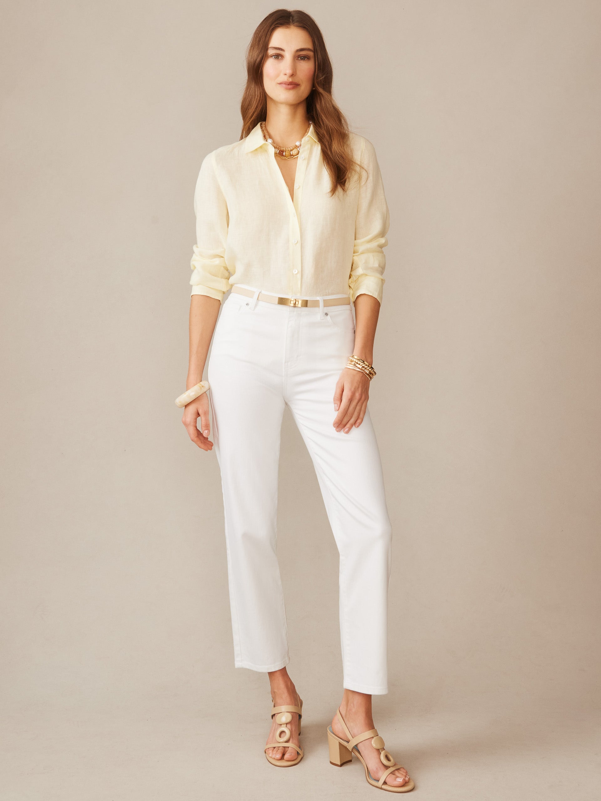 A woman models the Britt Linen Shirt by J.McLaughlin in a soft lemon hue, styled with white pants and beige sandals, showcasing effortlessly stylish and enduring designs.