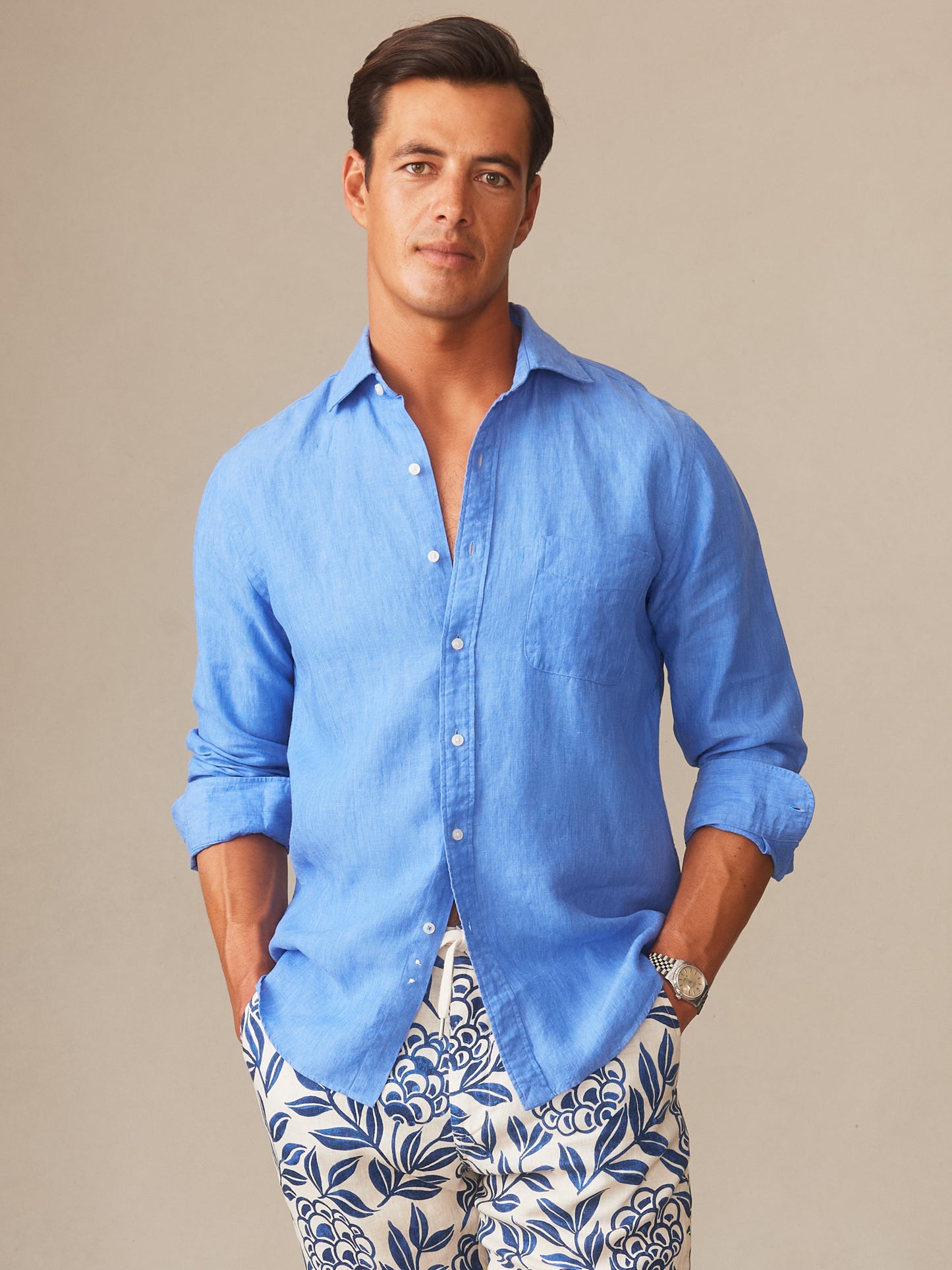 Man wearing a French blue Gramercy Linen Shirt by J.McLaughlin paired with patterned shorts, showcasing an effortlessly stylish look with enduring designs and innovative fabrics.