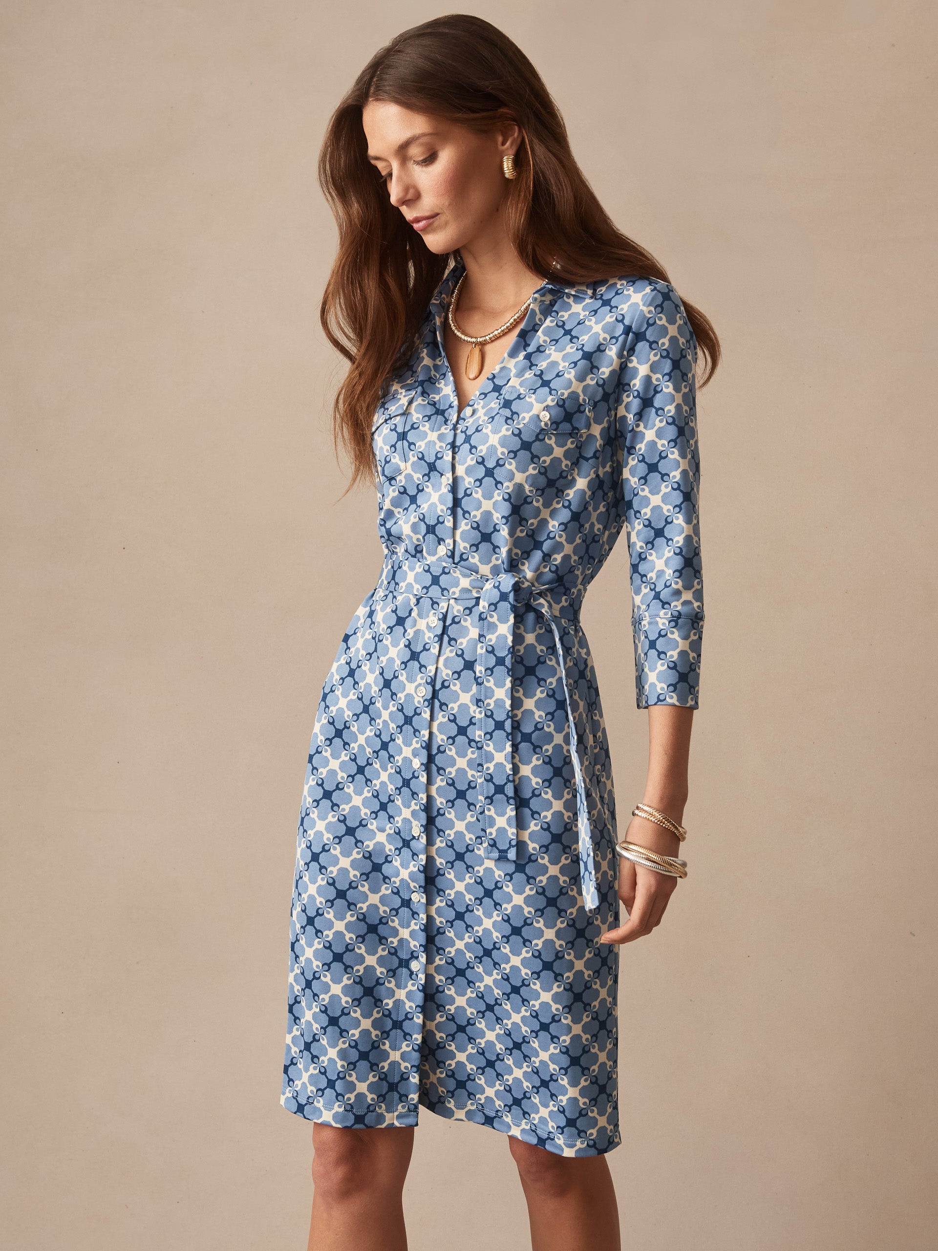 Woman wearing the Brynn Dress in Essex Geo by J.McLaughlin, a classic blue patterned dress with three-quarter sleeves and a waist tie, showcasing effortlessly stylish, enduring designs and innovative fabrics in a legacy of timeless fashion. A destination for defining style. Life, Well-Lived.