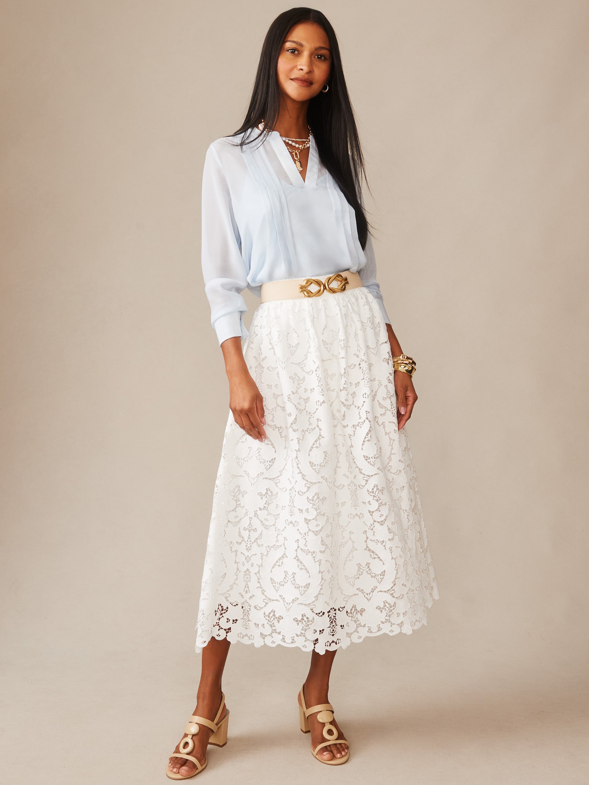 Woman wearing a light blue blouse paired with an off-white Callie Lace Skirt by J.McLaughlin, styled with beige sandals and gold accessories, showcasing effortlessly stylish, enduring designs.