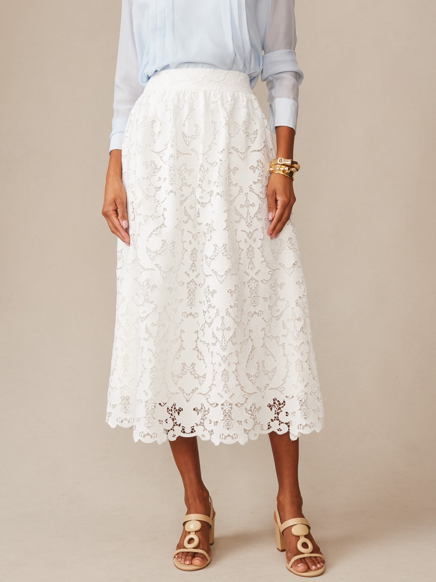 A model wearing the Callie Lace Skirt by J.McLaughlin in off-white, styled with a light blue blouse and beige sandals, showcasing effortlessly stylish, enduring designs and a legacy of timeless fashion.