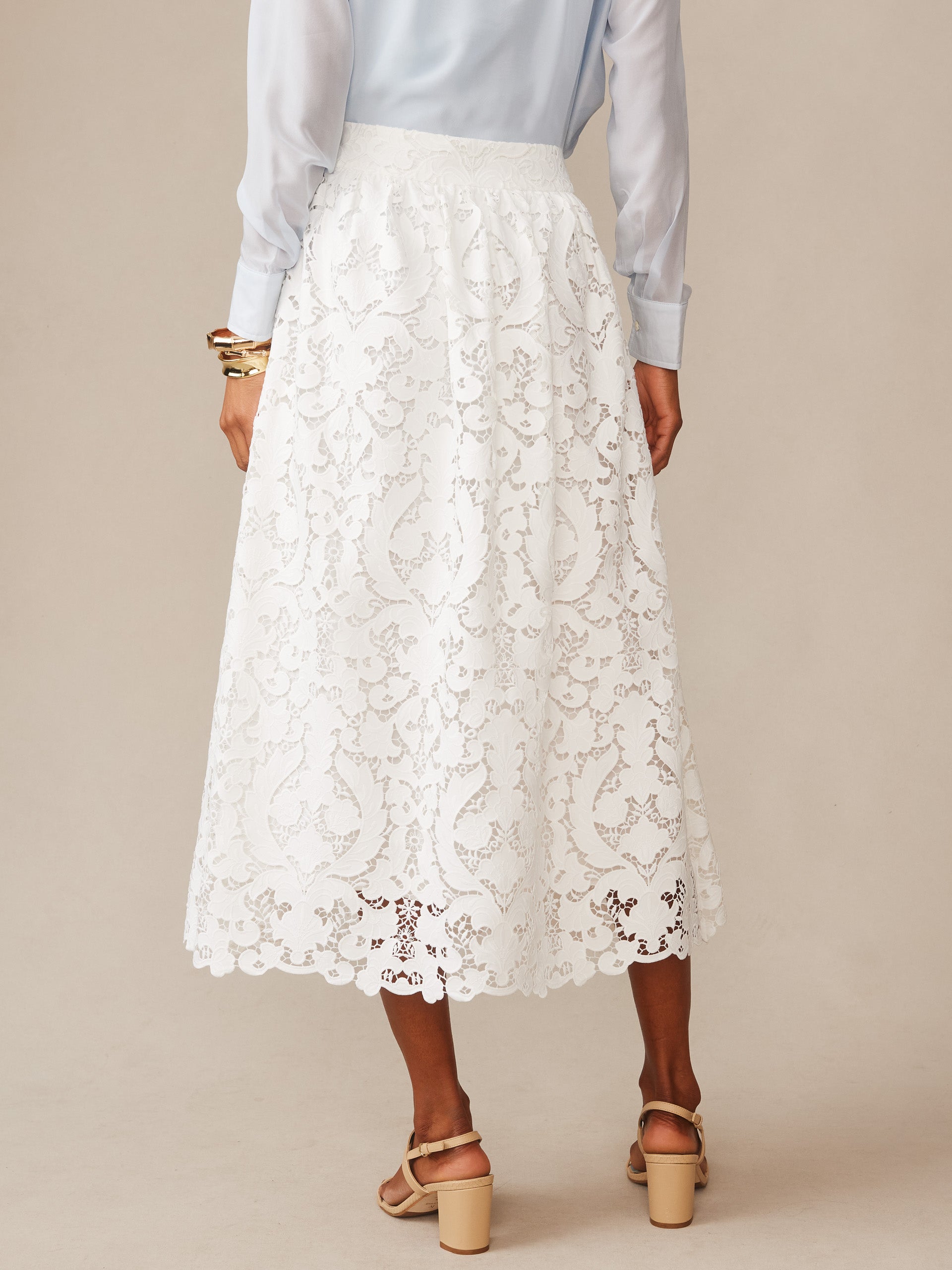 Woman wearing the J.McLaughlin Callie Lace Skirt in off-white, showcasing intricate lace patterns and a classic midi length, embodying effortlessly stylish and enduring designs.