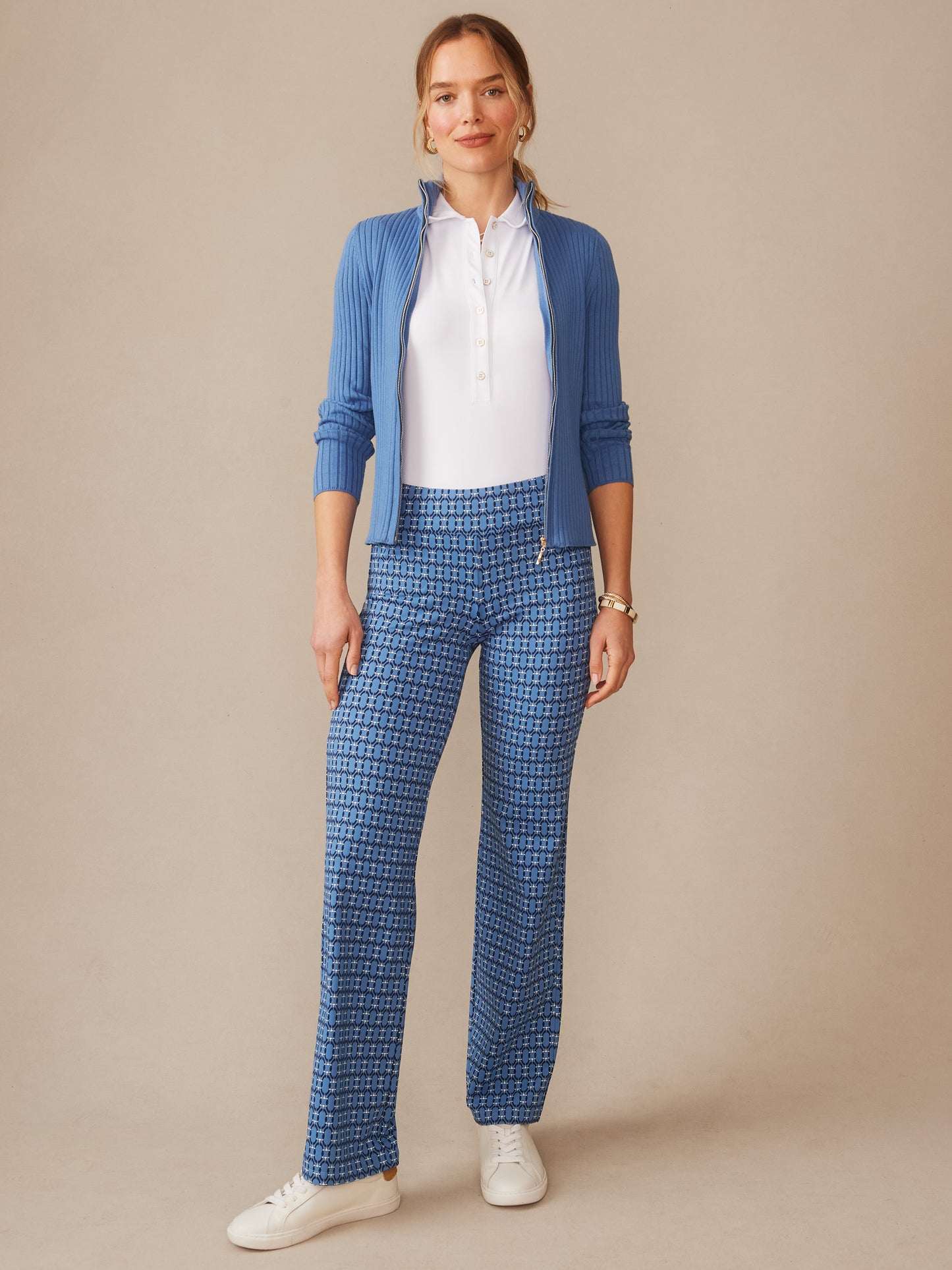 A woman wearing J.McLaughlin Carmel Pants in Signet Lock paired with a white polo and blue zip-up cardigan, showcasing effortlessly stylish, enduring designs and innovative fabrics.