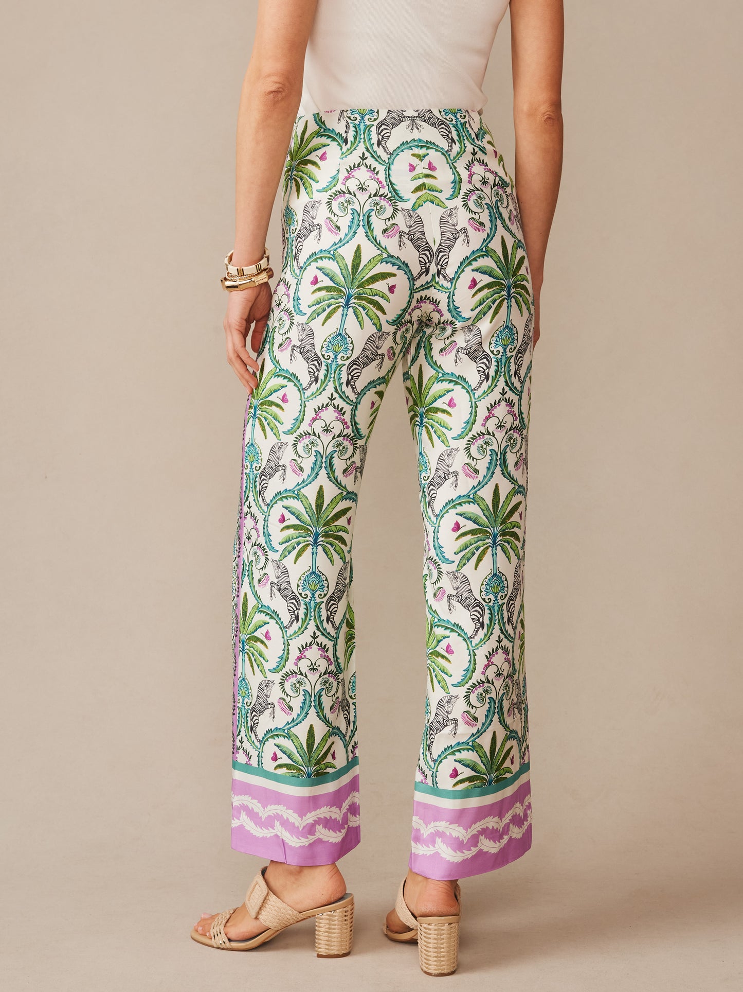 Woman wearing Carter Silk Blend Pants in Zebra Isle Edge by J.McLaughlin, featuring a vibrant tropical print with palm motifs and lavender border, effortlessly stylish and crafted with innovative fabrics for enduring designs in a legacy of timeless fashion, a destination for defining style. Life, Well-Lived.