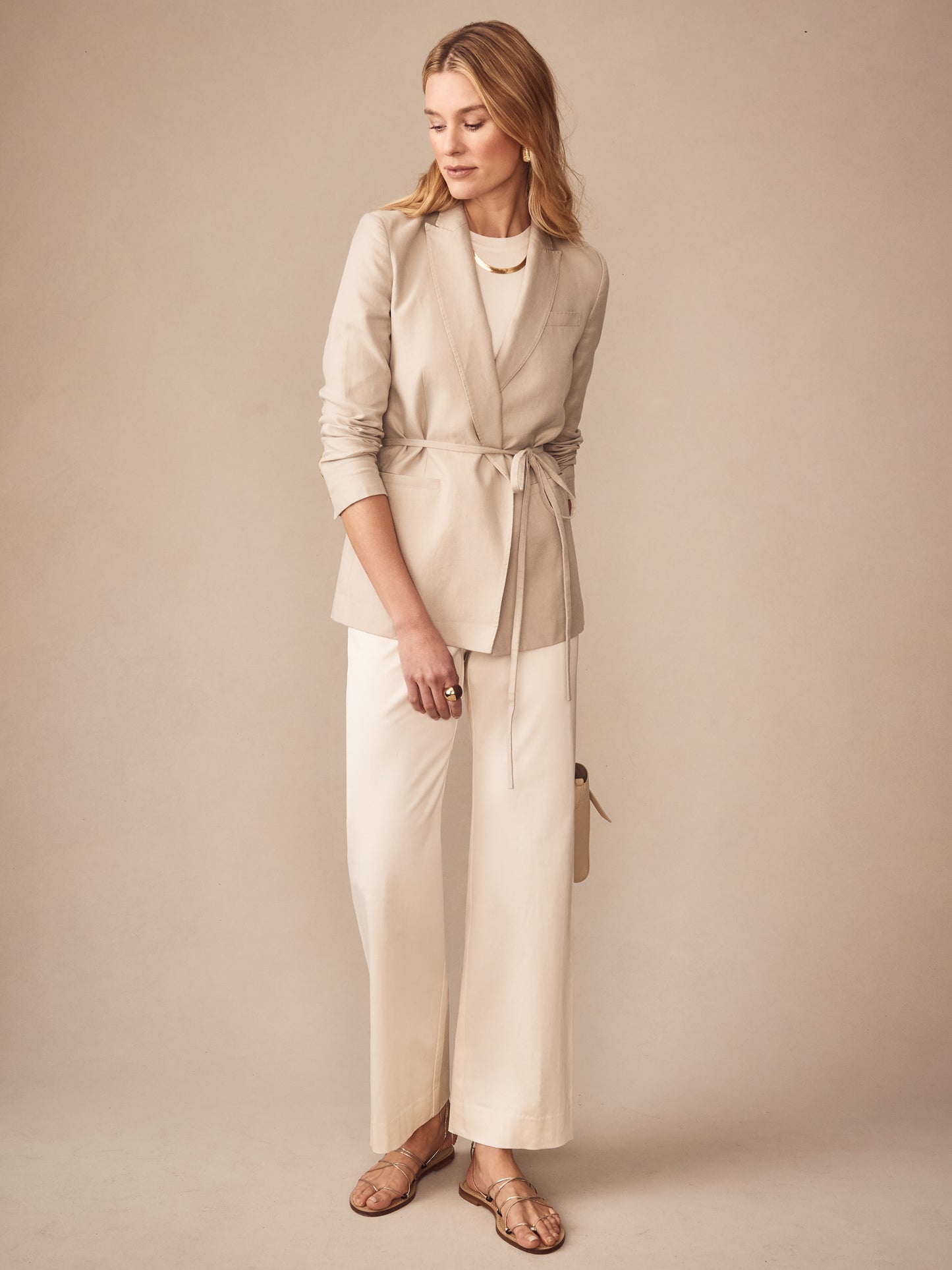 Woman wearing cream-colored Carter Dupioni Cotton Pants paired with a beige belted blazer, sandals, and gold jewelry, showcasing J.McLaughlin’s effortlessly stylish, enduring designs.