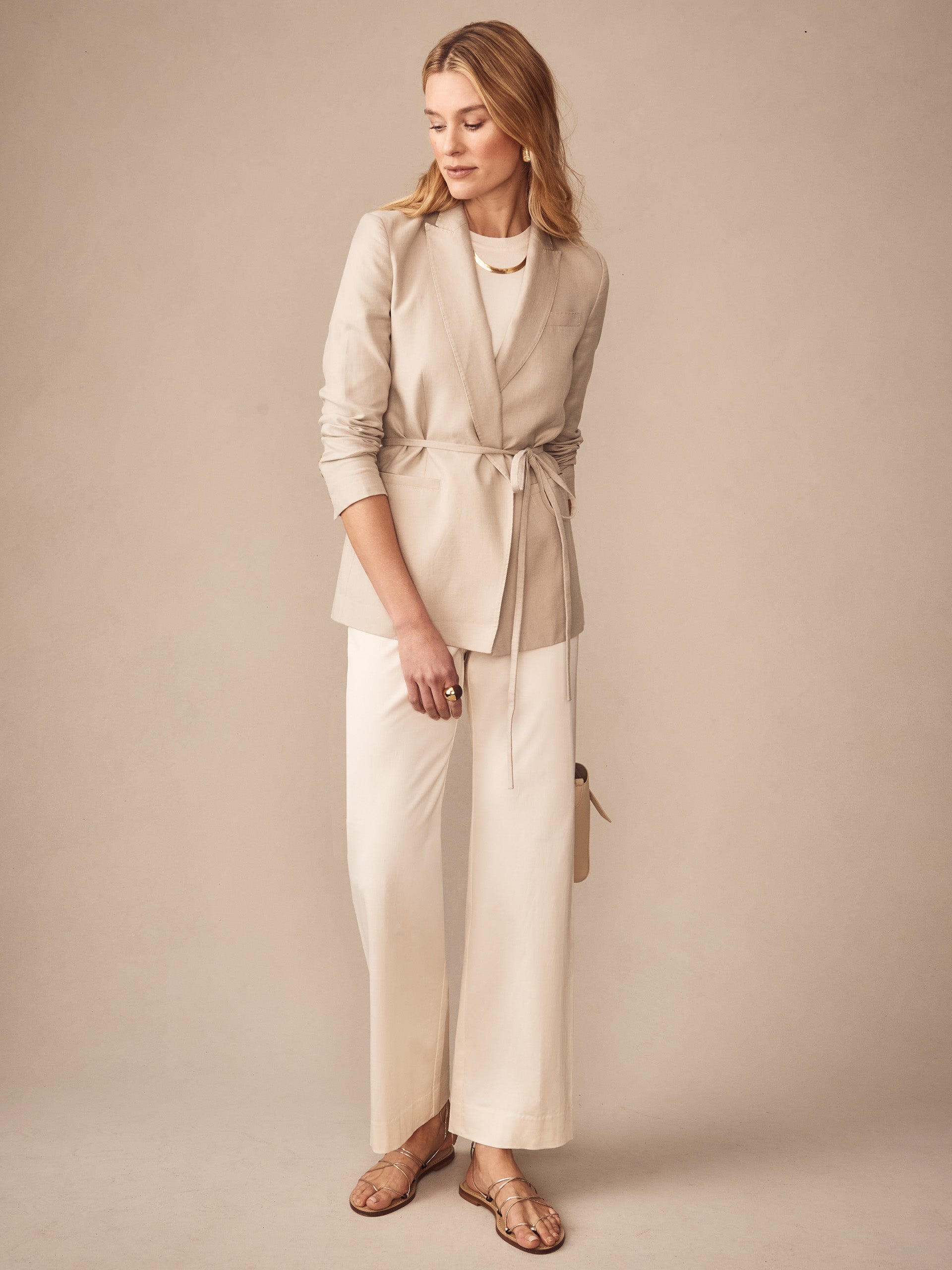 Woman wearing cream-colored Carter Dupioni Cotton Pants paired with a beige belted blazer, sandals, and gold jewelry, showcasing J.McLaughlin’s effortlessly stylish, enduring designs.