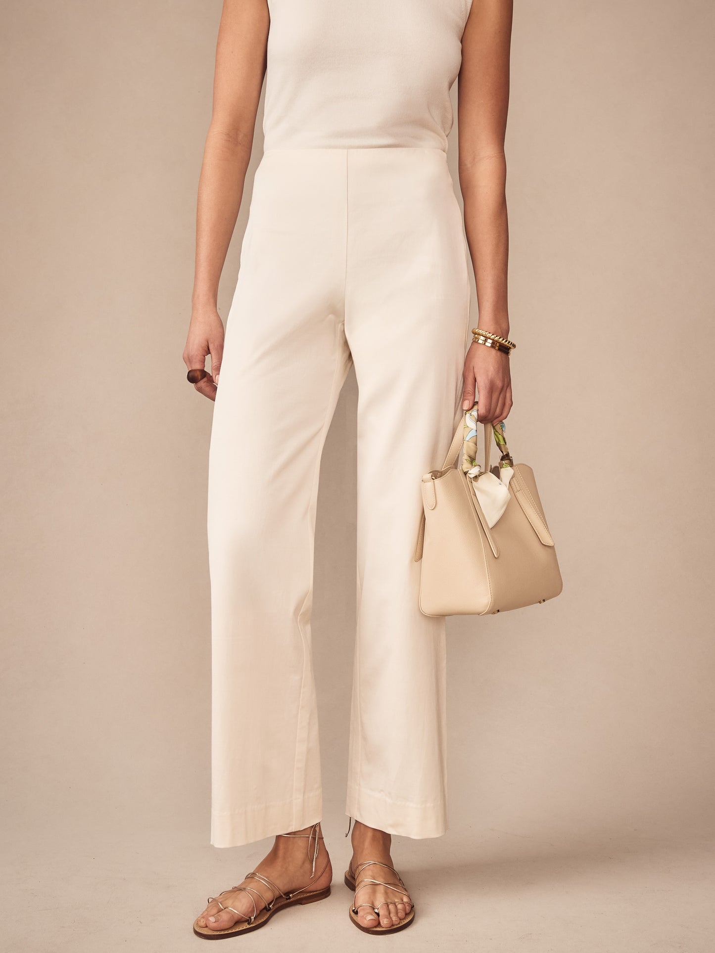 Woman wearing cream Carter Dupioni Cotton Pants from J.McLaughlin paired with a sleeveless top and beige handbag, showcasing effortlessly stylish, enduring designs and innovative fabrics.