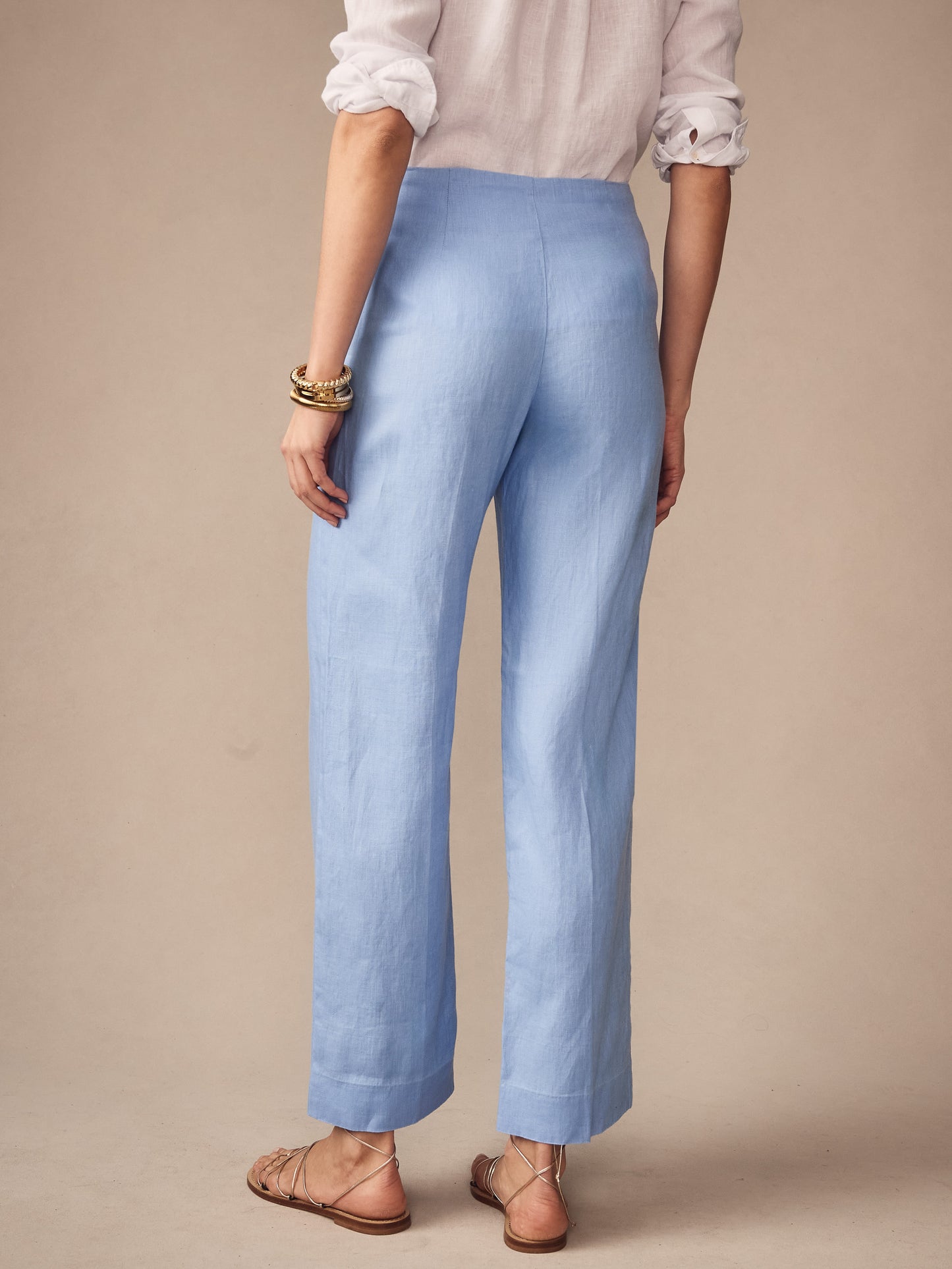 Woman seen from the back wearing J. McLaughlin Carter Linen Pants in a soft cornflower blue, paired with a lightweight white blouse and sandals, showcasing effortlessly stylish, enduring designs.