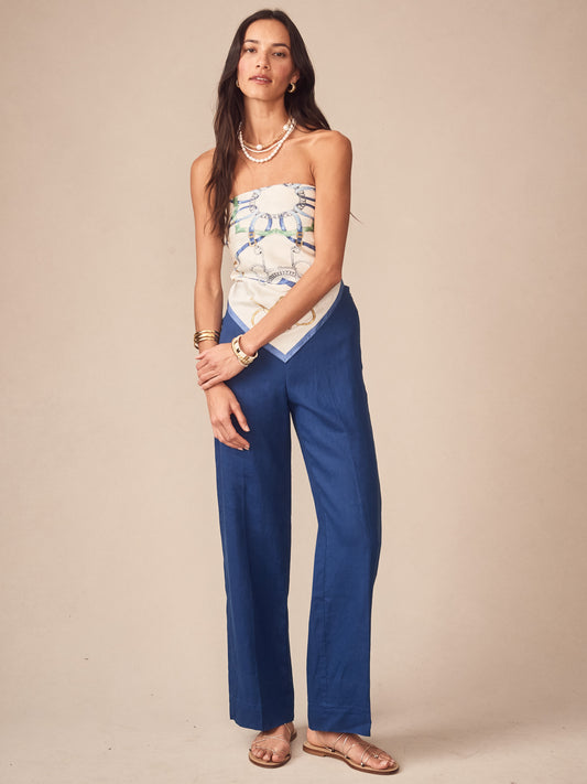 Woman wearing J.McLaughlin Carter Linen Pants in navy paired with a light patterned strapless top, accessorized with layered necklaces and gold bracelets, showcasing effortlessly stylish, enduring designs with innovative fabrics. A destination for defining style. Life, Well-Lived.