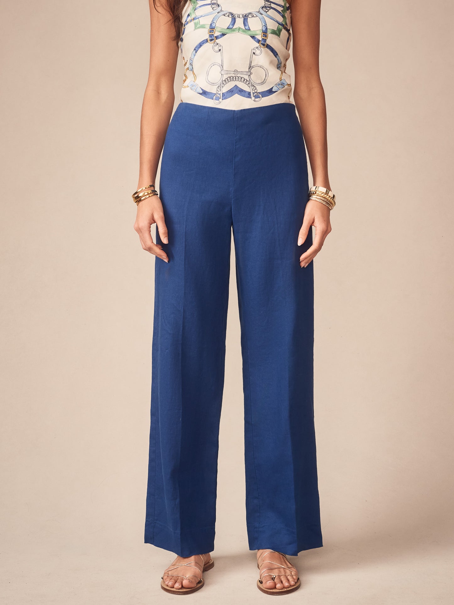 Woman wearing J.McLaughlin Carter Linen Pants in a rich navy hue paired with a stylish patterned sleeveless top and gold bangles, showcasing effortlessly stylish and enduring designs.