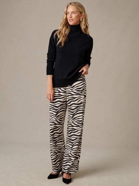 J.McLaughlin Carter Pants in Zebra Stripes modeled with a black turtleneck sweater and black shoes showcasing tailored cream and black striped pants
