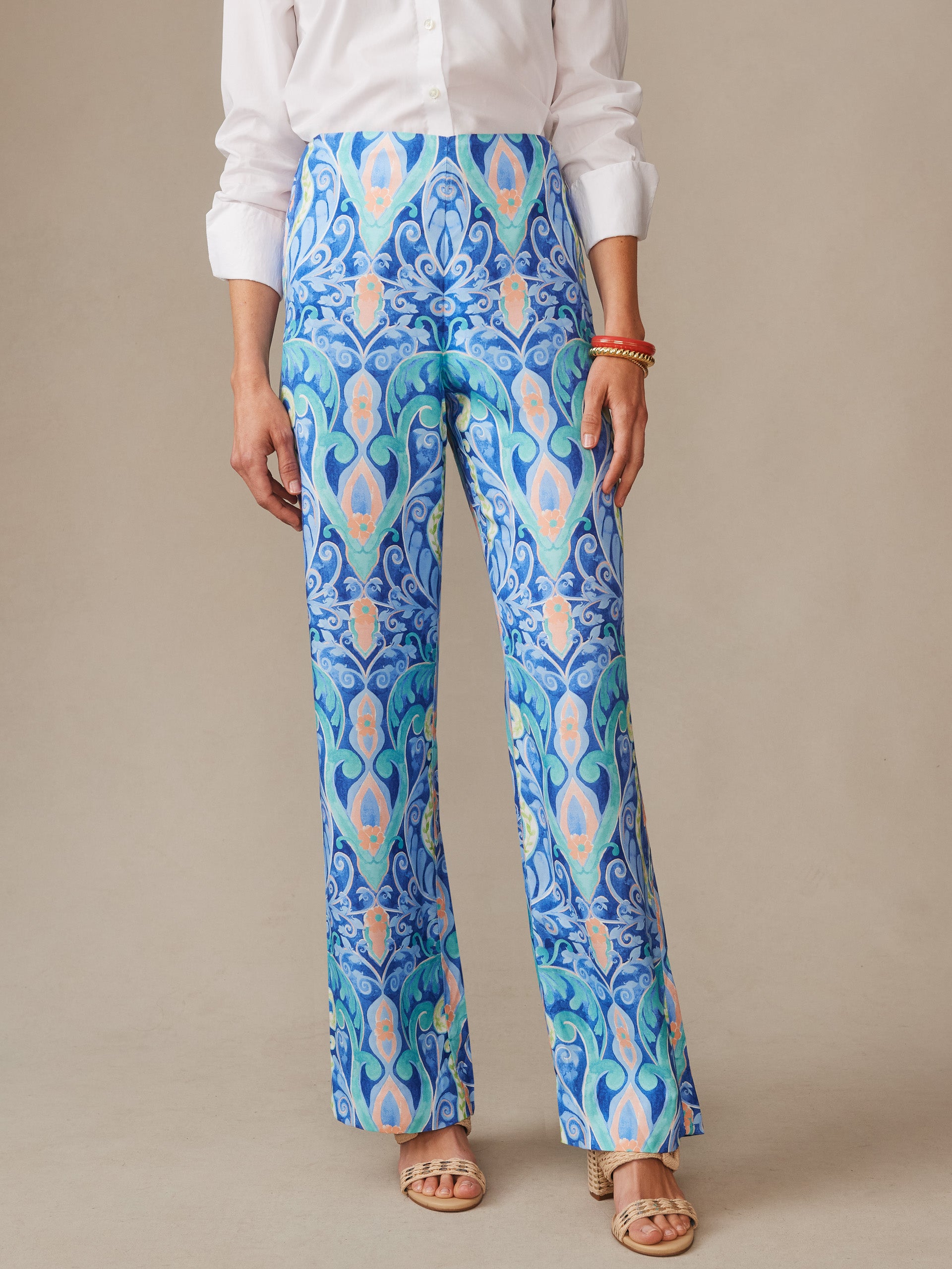 Woman wearing Carter Silk Blend Pants in Mini Deco Bloom by J.McLaughlin, featuring an intricate blue and aqua pattern, paired with a white blouse and stylish sandals, showcasing effortlessly stylish enduring designs with innovative fabrics, a destination for defining style. Life, Well-Lived.