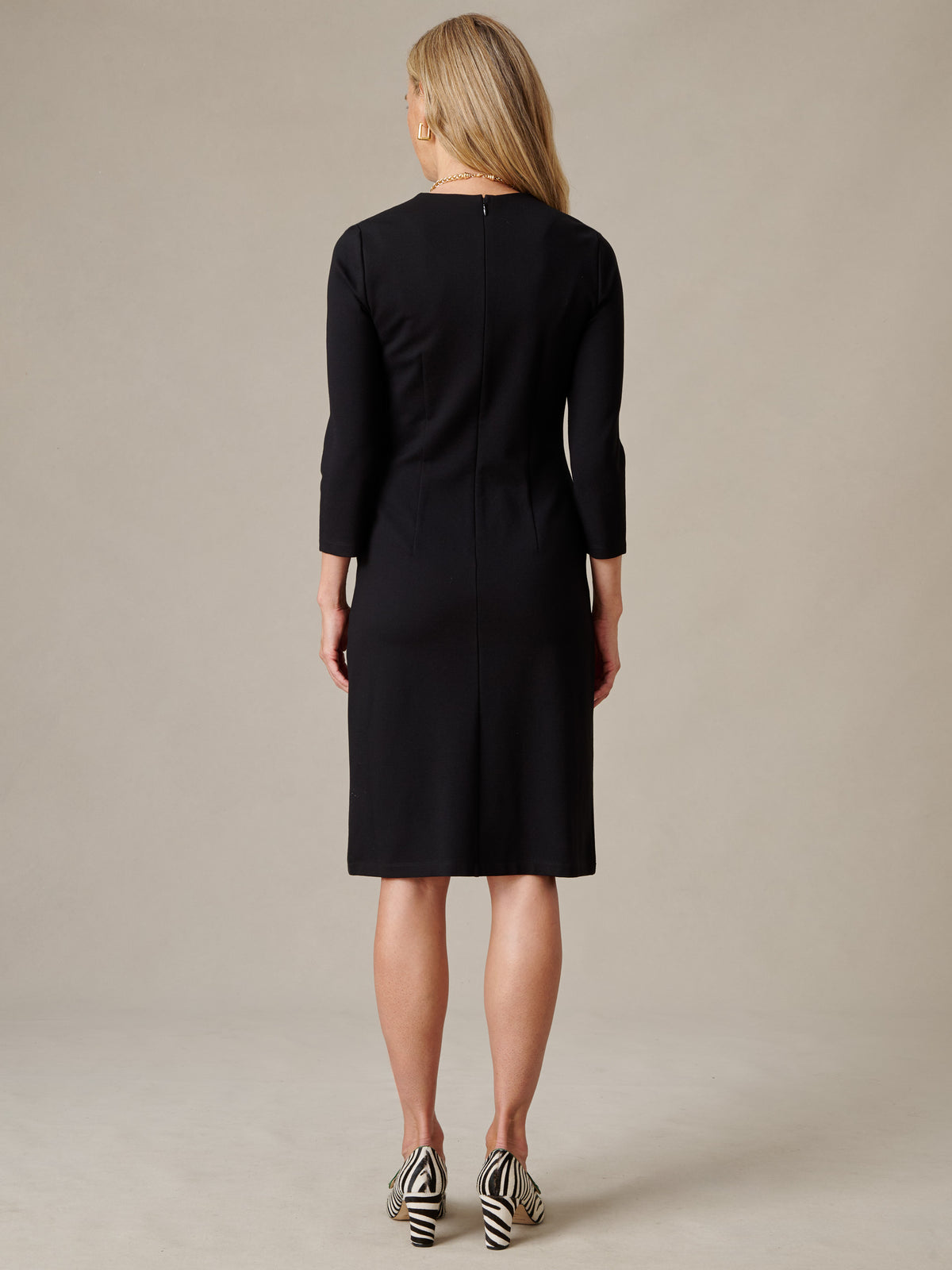 J.McLaughlin Catalyst Dress shown from the back on a model wearing a tailored black knit dress with long sleeves and striped heels