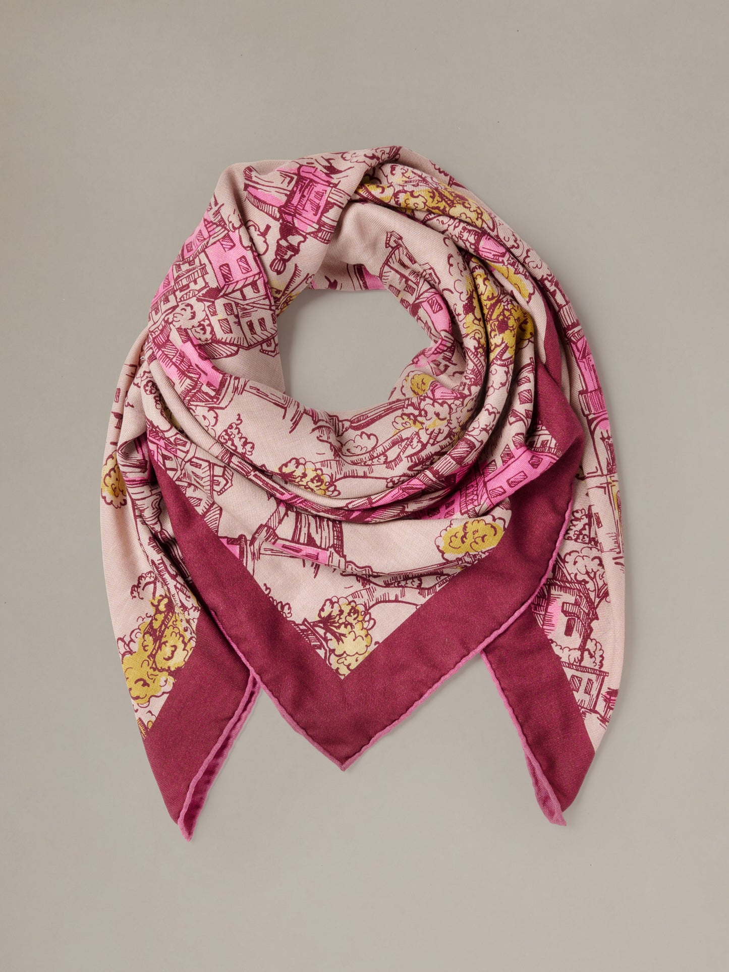 The Charlotte Scarf in Boulevard Sketch Border by J.McLaughlin shown draped in a soft pink cashmere silk blend with burgundy and gold illustrated motifs