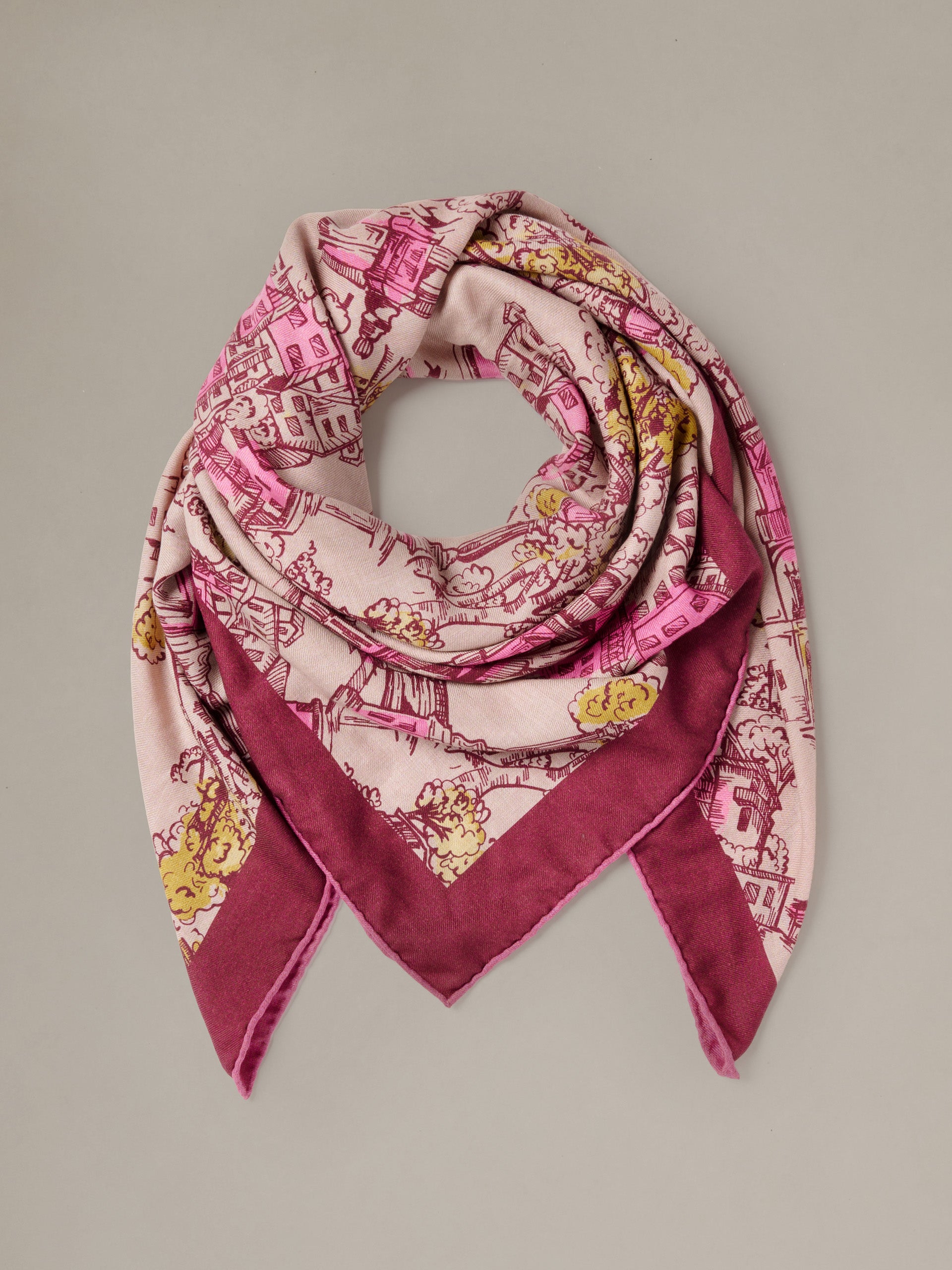 The Charlotte Scarf in Boulevard Sketch Border by J.McLaughlin shown draped in a soft pink cashmere silk blend with burgundy and gold illustrated motifs