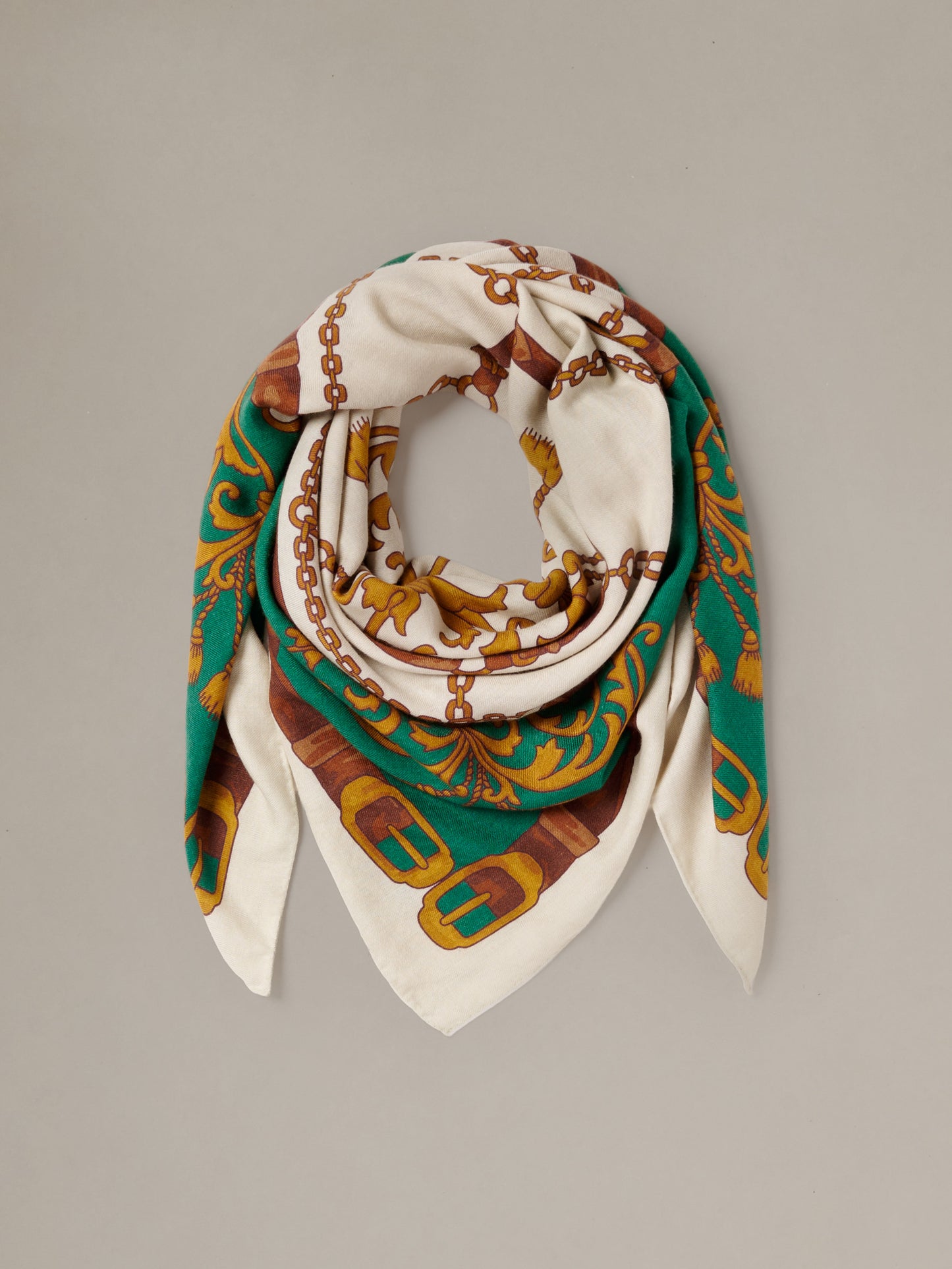 The Charlotte Scarf in Gilded Bridle Border by J.McLaughlin shown draped in a loop with a cream base and ornate green brown and gold bridle motif