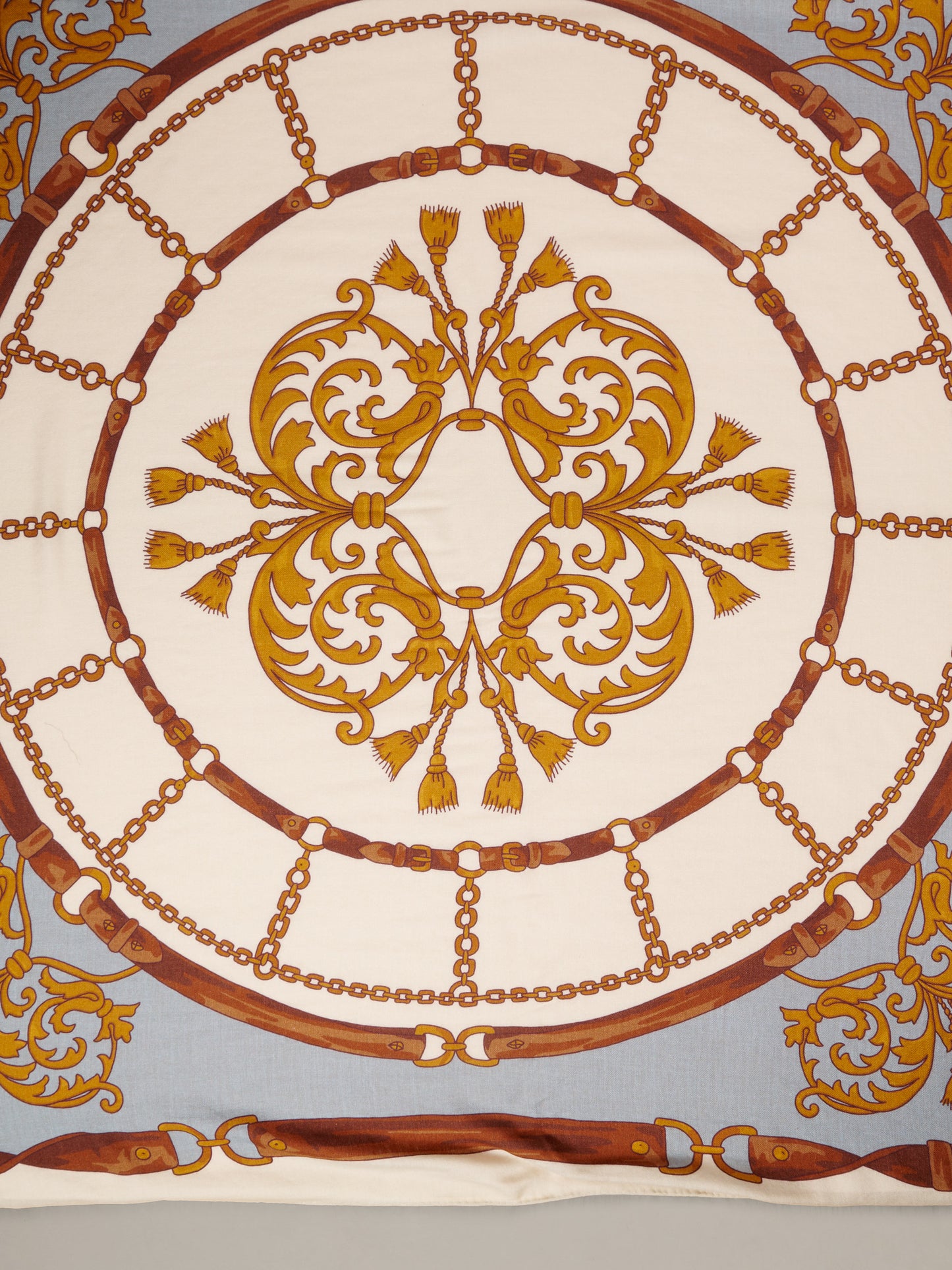 The Charlotte Scarf in Gilded Bridle Border by J.McLaughlin featuring an ornate cream scarf with gold and brown bridle chain motifs