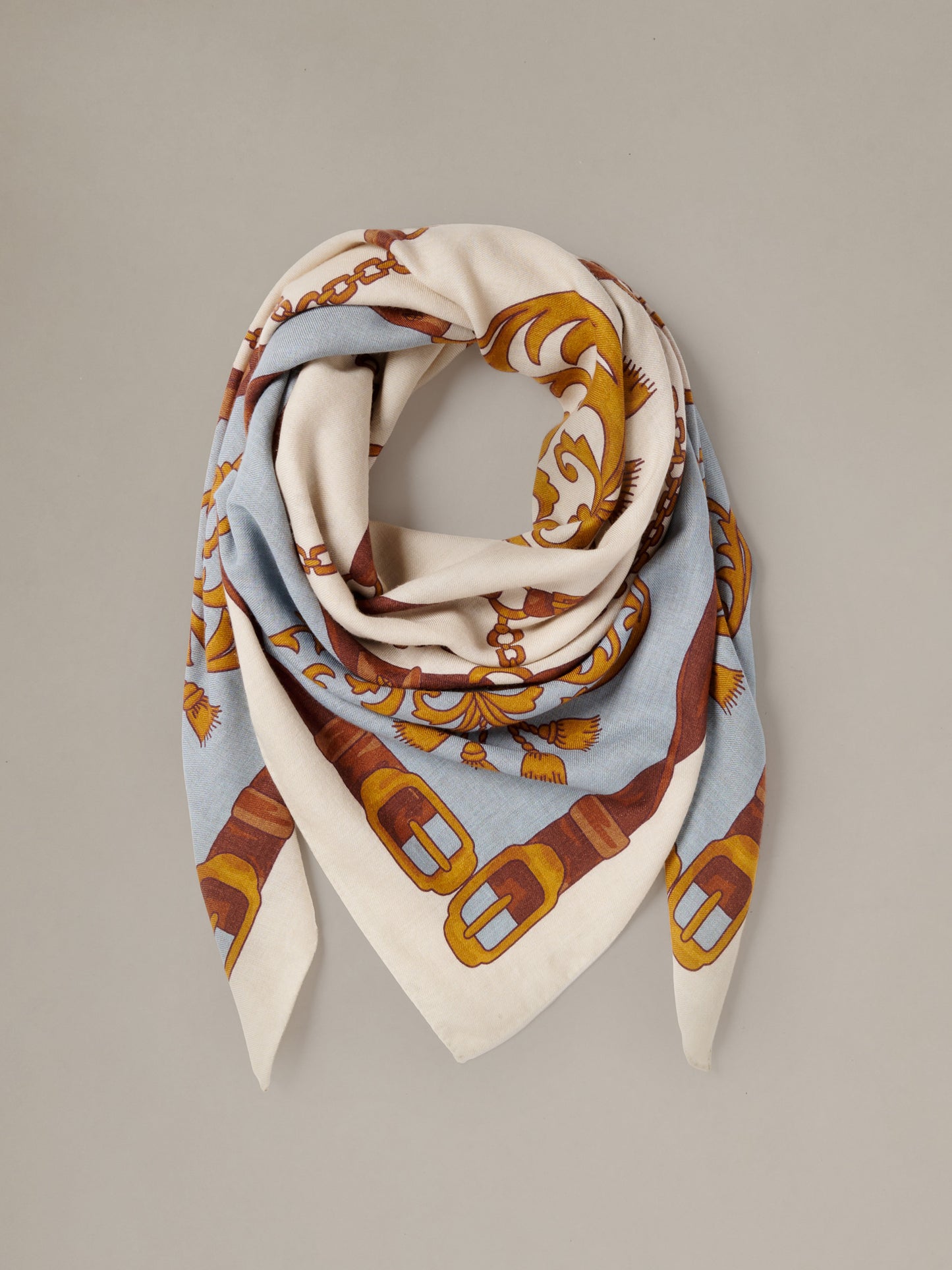 The Charlotte Scarf in Gilded Bridle Border by J.McLaughlin draped in cream and pale blue with ornate gilded bridle motifs and brown accents